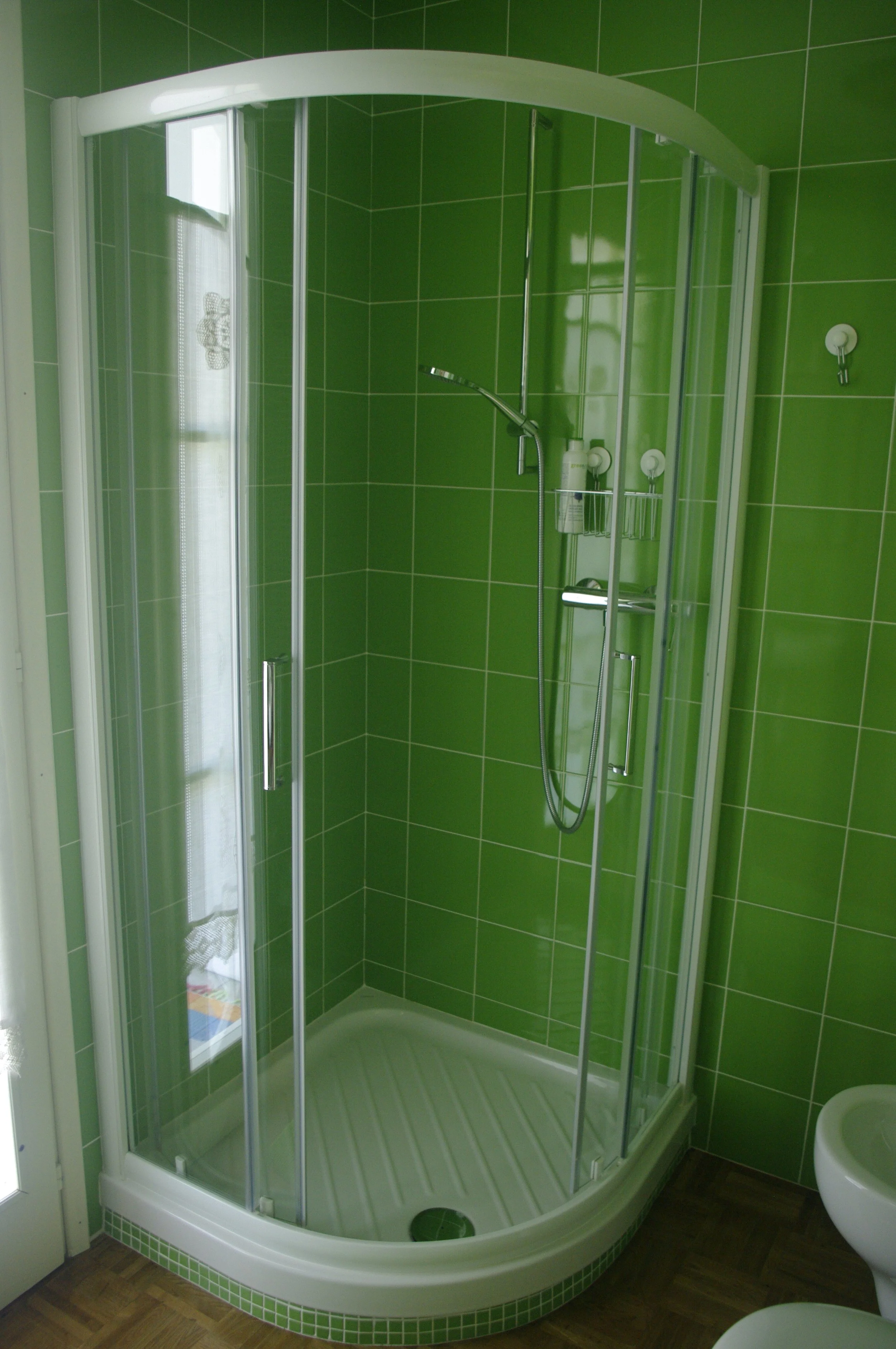 Doccia con pareti di vetro e piastrelle verdi in un bagno, con parete finestrata e mobili bianco.