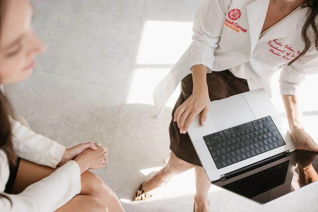 Medical professional holding a laptop and consulting with a patient in a clinic.