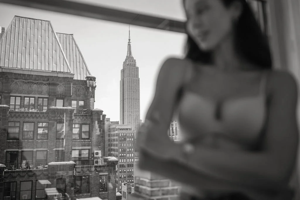 A blurred woman standing near a window with a view of the Empire State Building in New York City.