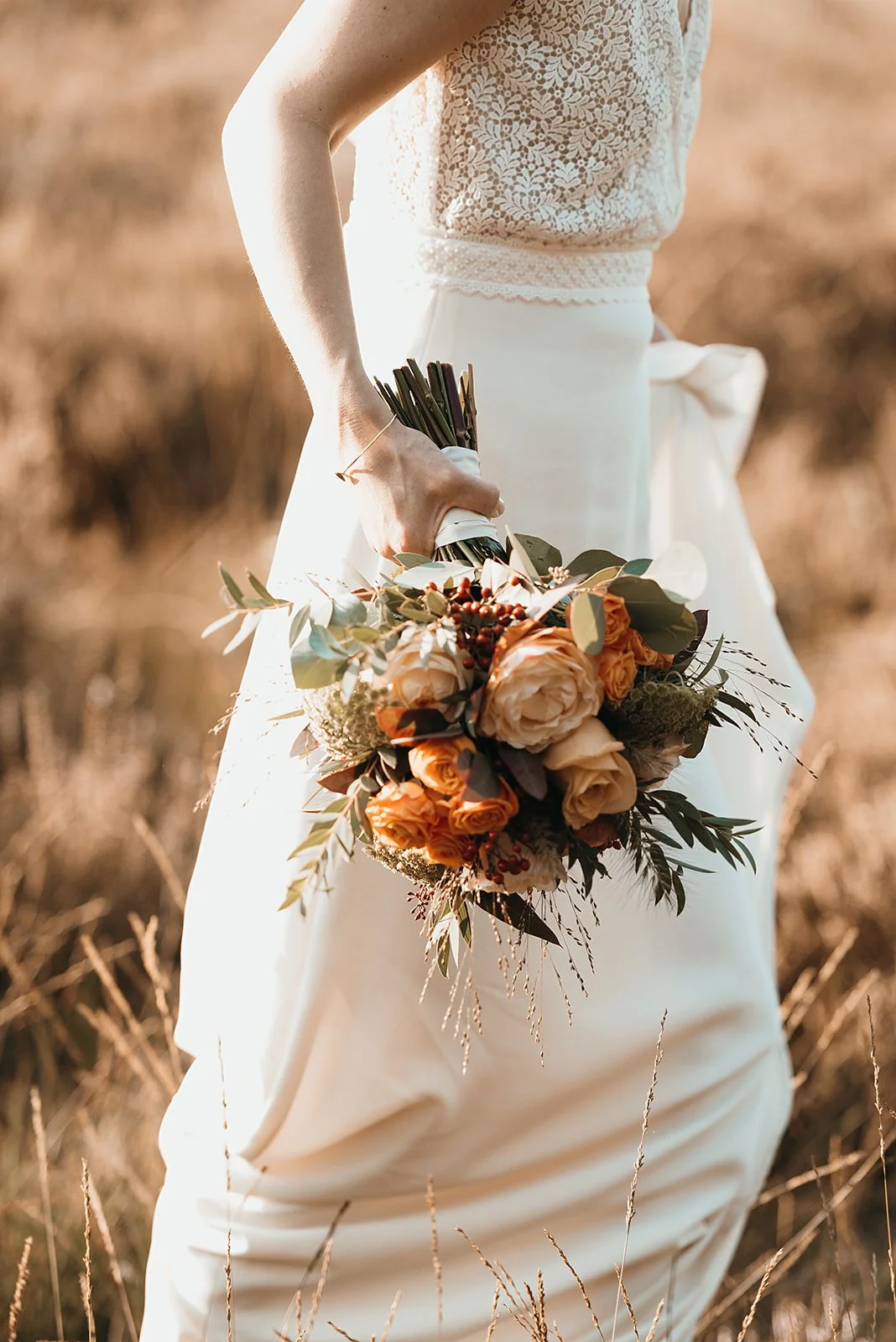 A woman in a lace top and long skirt holding a bouquet of roses and greenery outdoors.