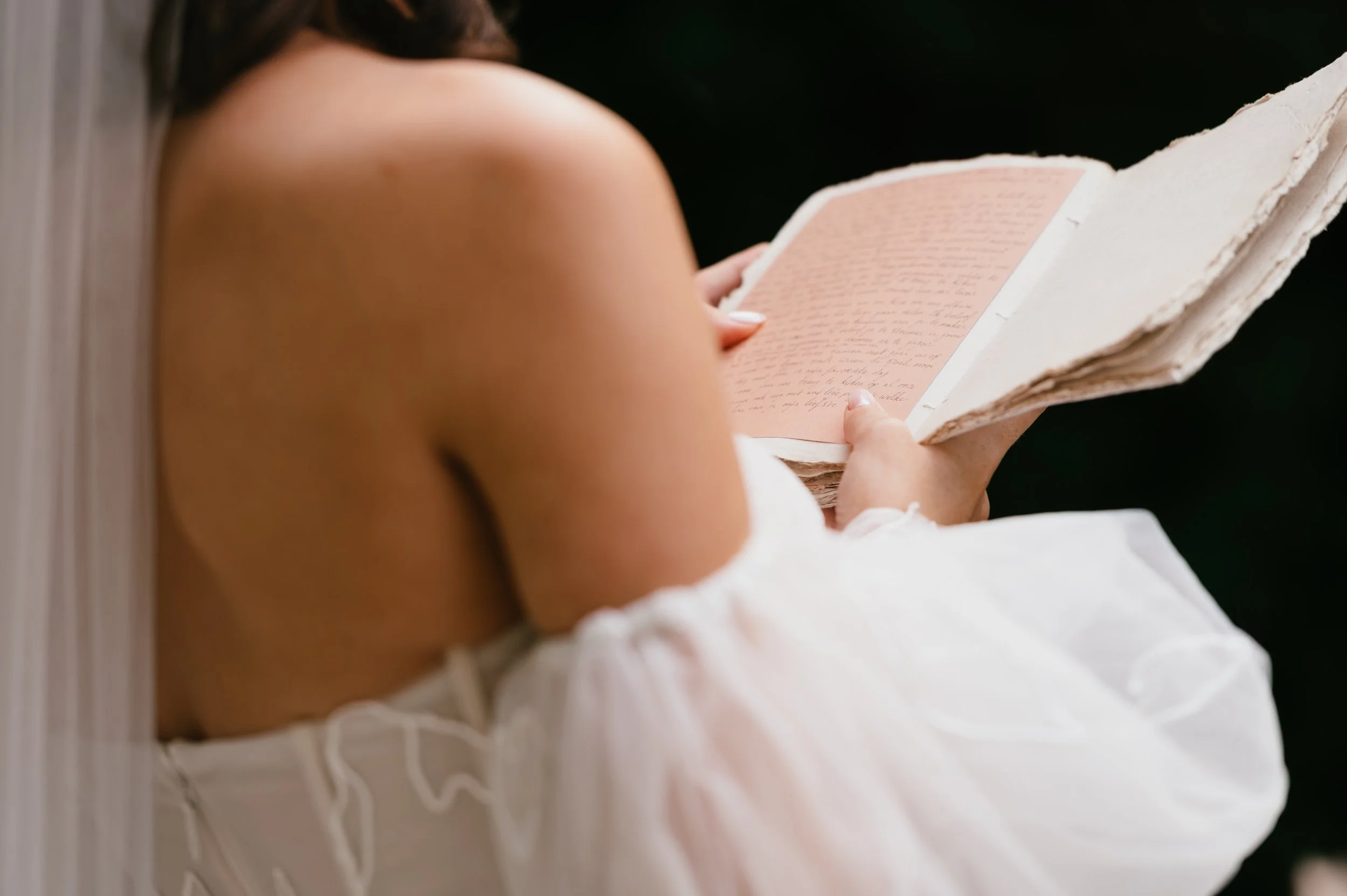 Bride reading an old, textured book with handwritten text, wearing an off-shoulder white dress.