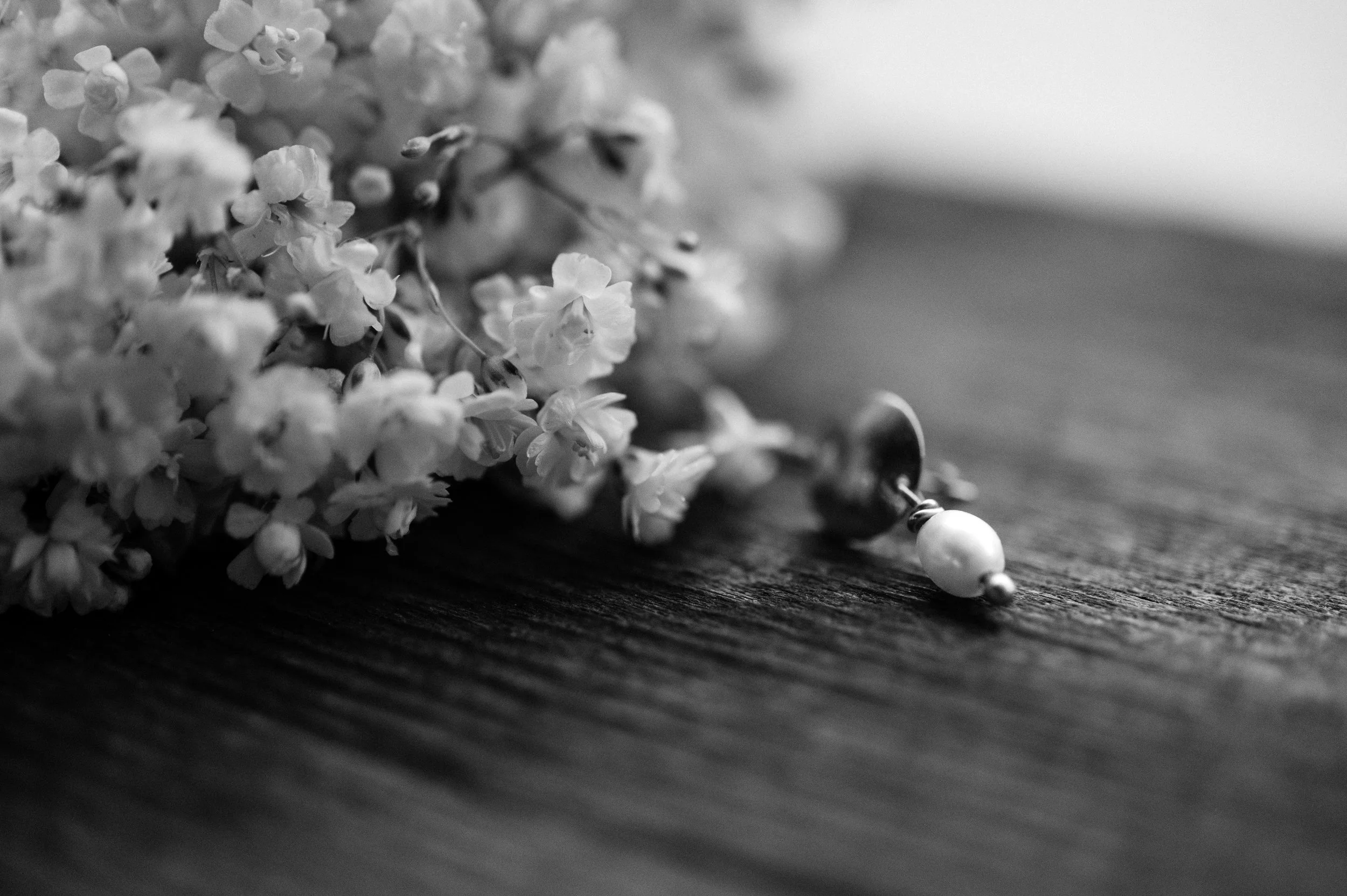 Black and white close-up of small white flowers with a pearl and metallic earring on a dark textured surface.