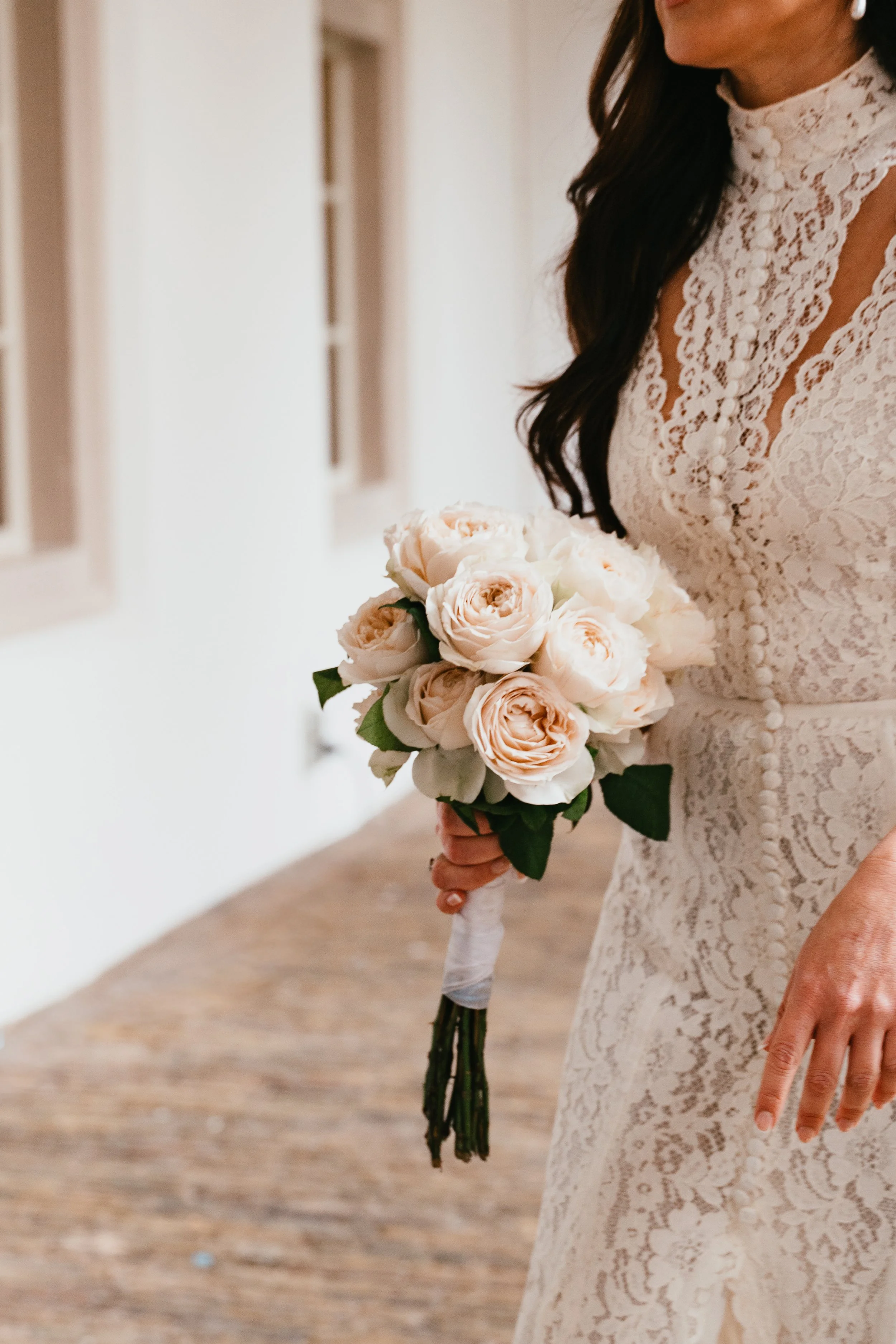 A bride in a lace wedding dress holding a bouquet of pale pink roses.