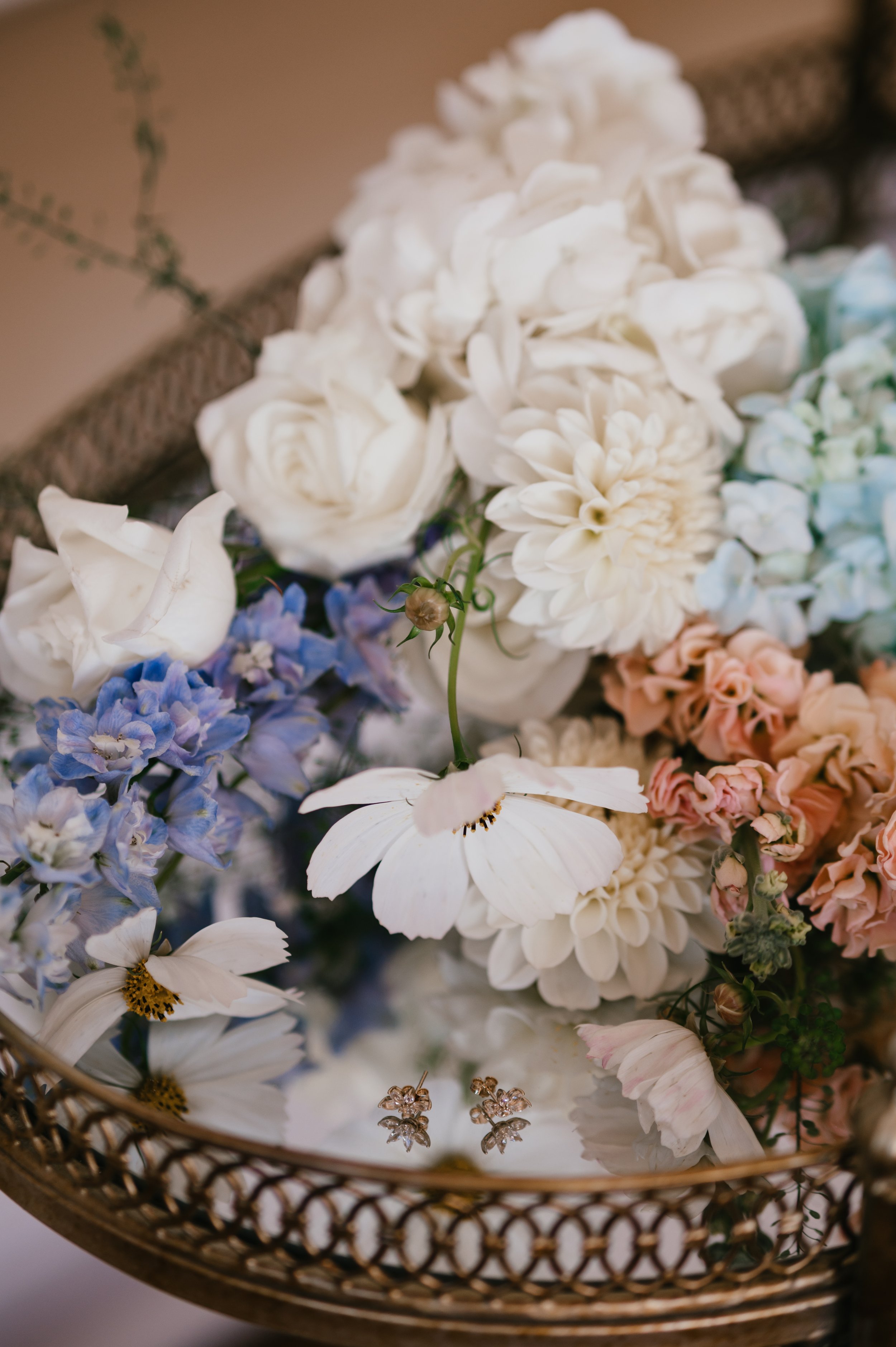 A decorative tray filled with white, blue, and peach floral arrangements and a pair of small flower-shaped earrings.
