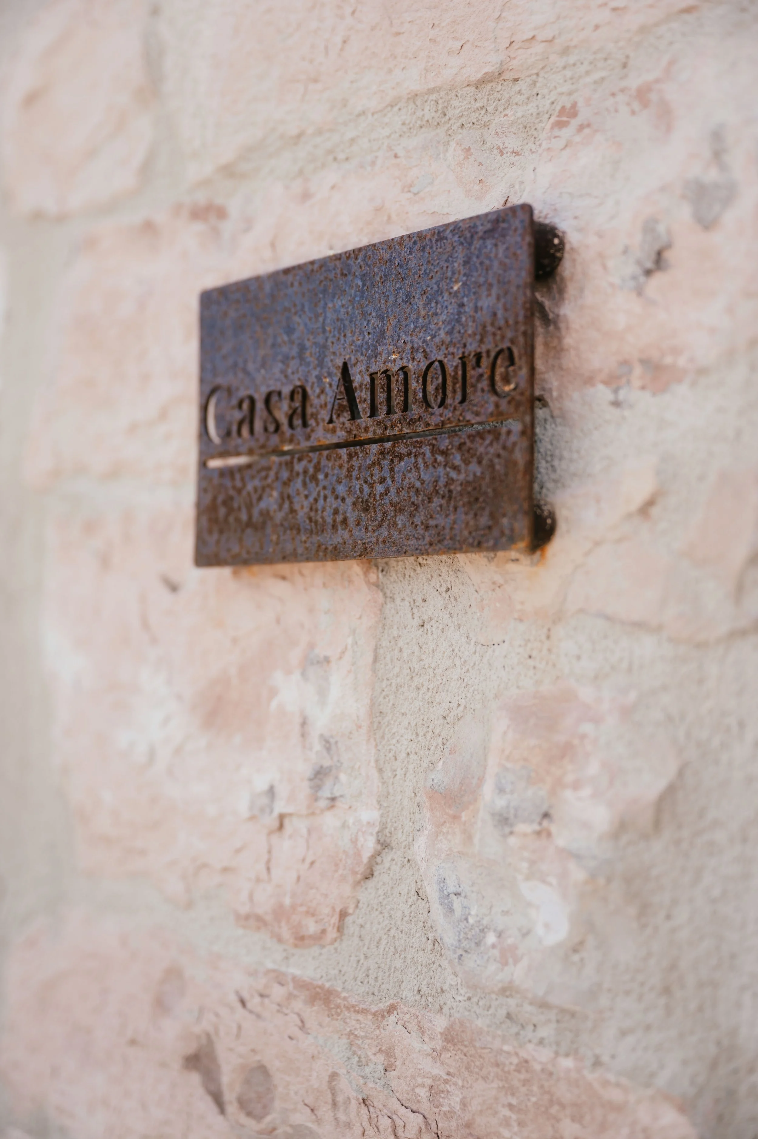 A rusted metal plaque reading 'Casa Amore' mounted on a textured beige stone wall.