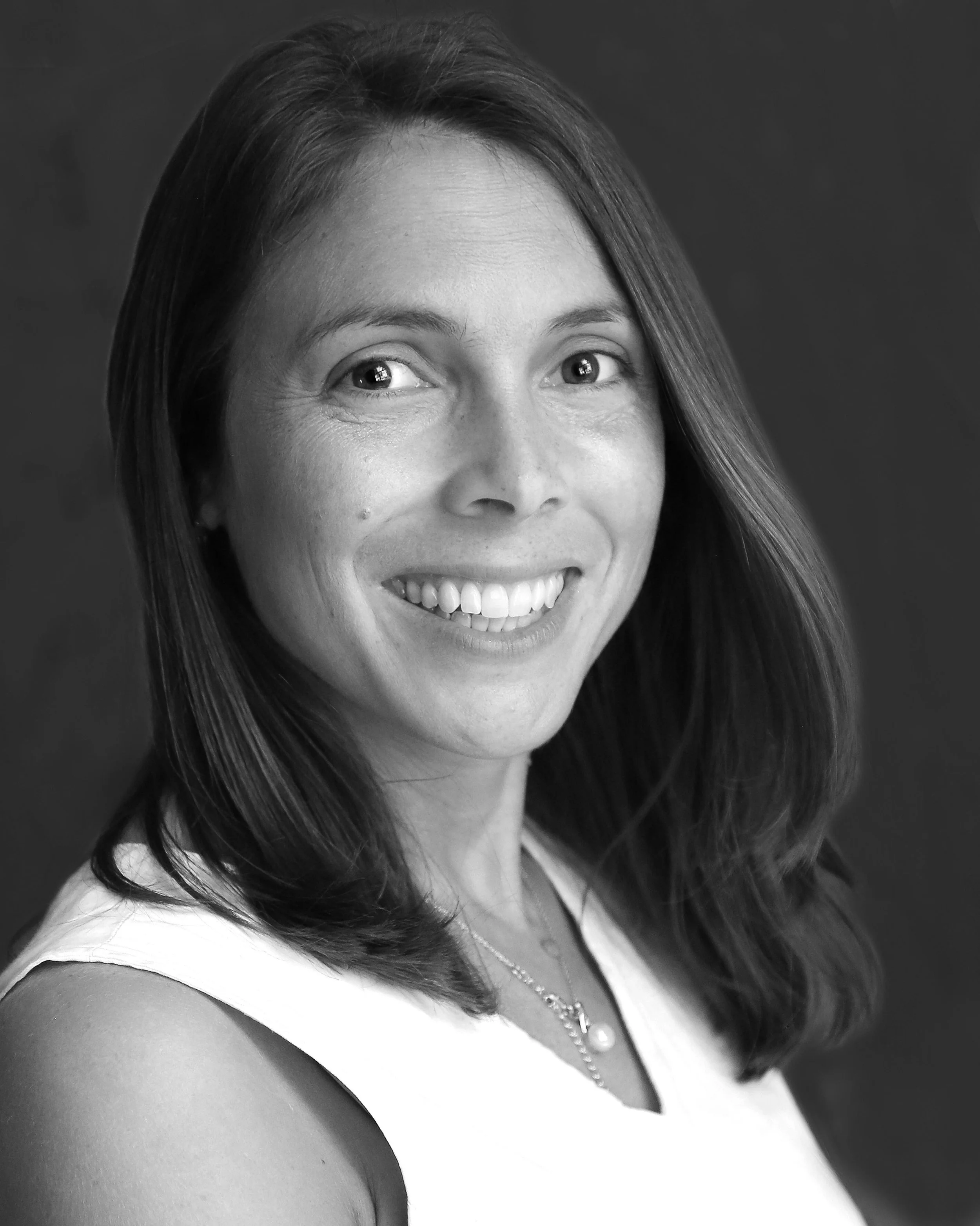 Black and white portrait of a woman smiling, with shoulder-length hair, wearing a sleeveless top and a pearl necklace.