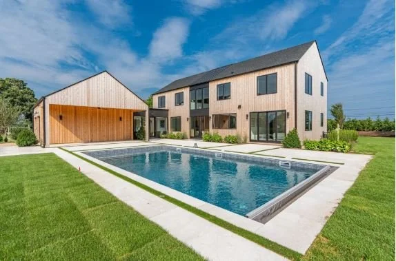 Modern two-story house with a swimming pool in the backyard, surrounded by green grass and a clear blue sky.