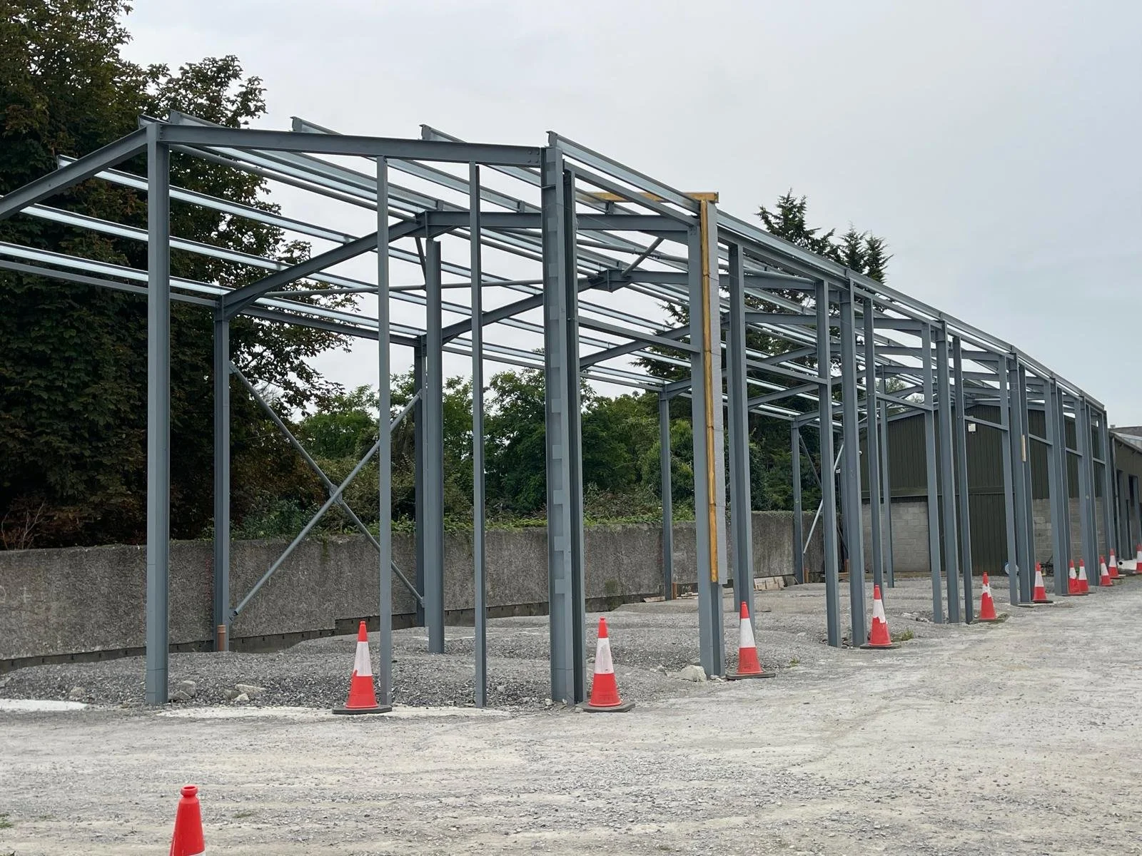 Steel framing for a building under construction with orange traffic cones along the perimeter.