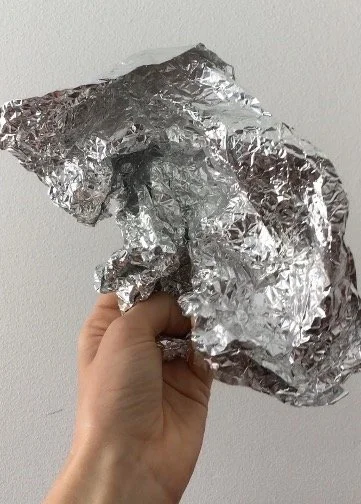 A hand holding crumpled aluminum foil against a plain wall 
