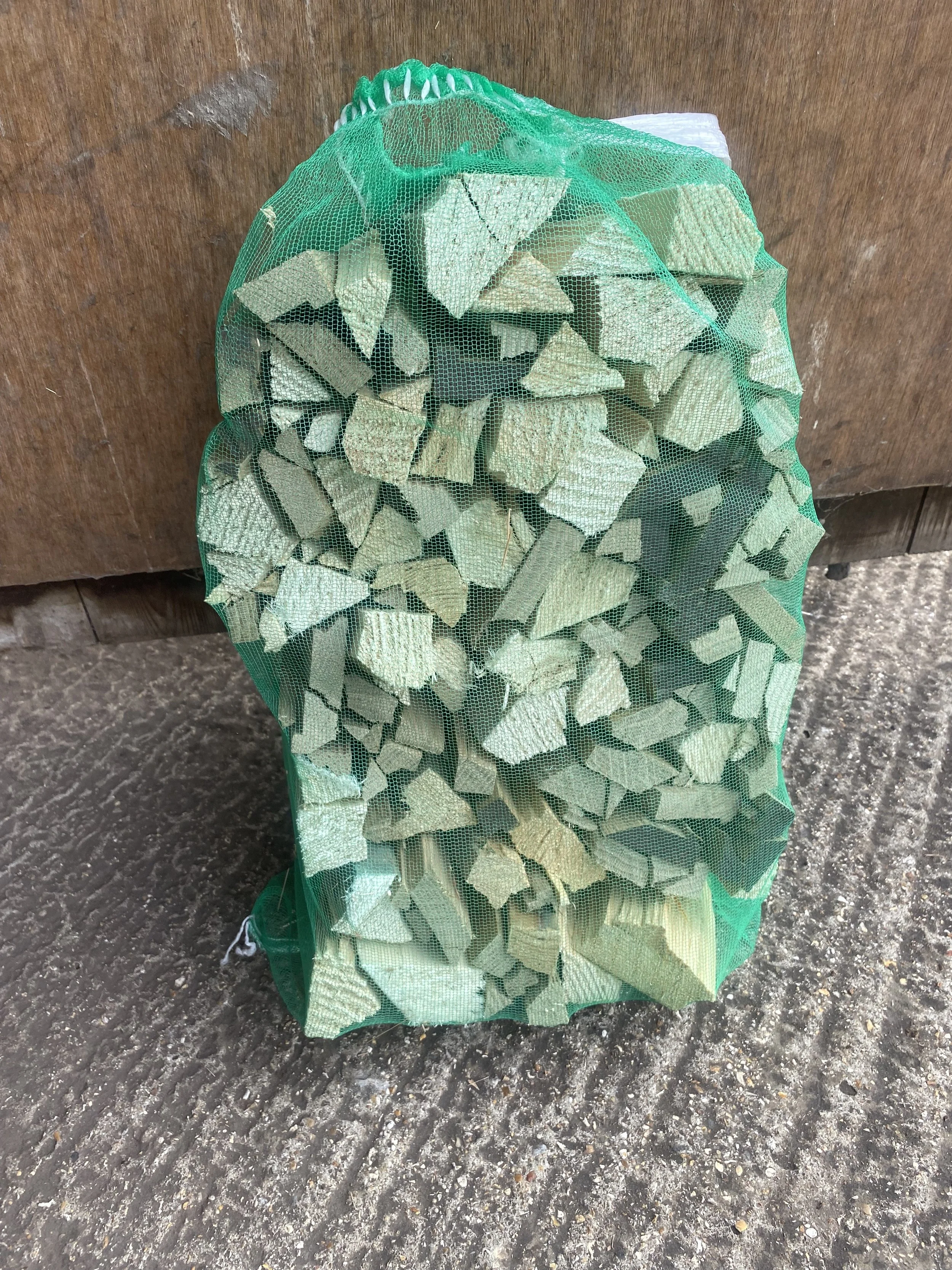 A green mesh bag filled with chopped firewood pieces.