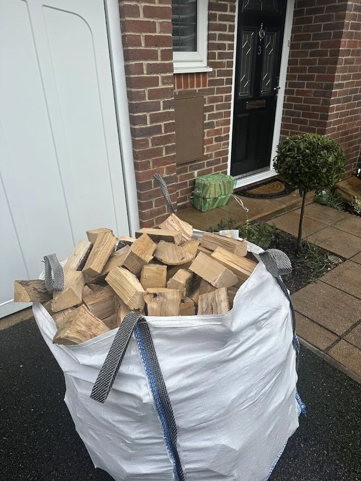 Bag filled with chopped firewood outside a brick house near the front door.