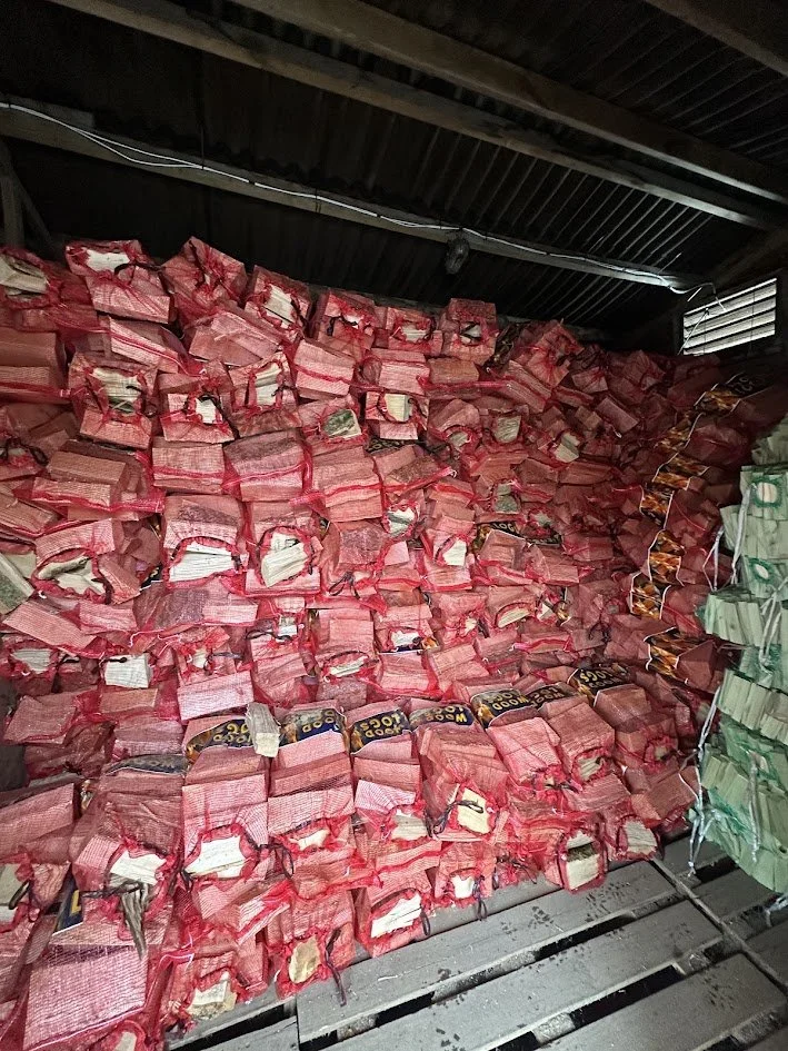 Large pile of red mesh bags filled with blocks of logs, stacked on a metal surface in a warehouse or storage area.