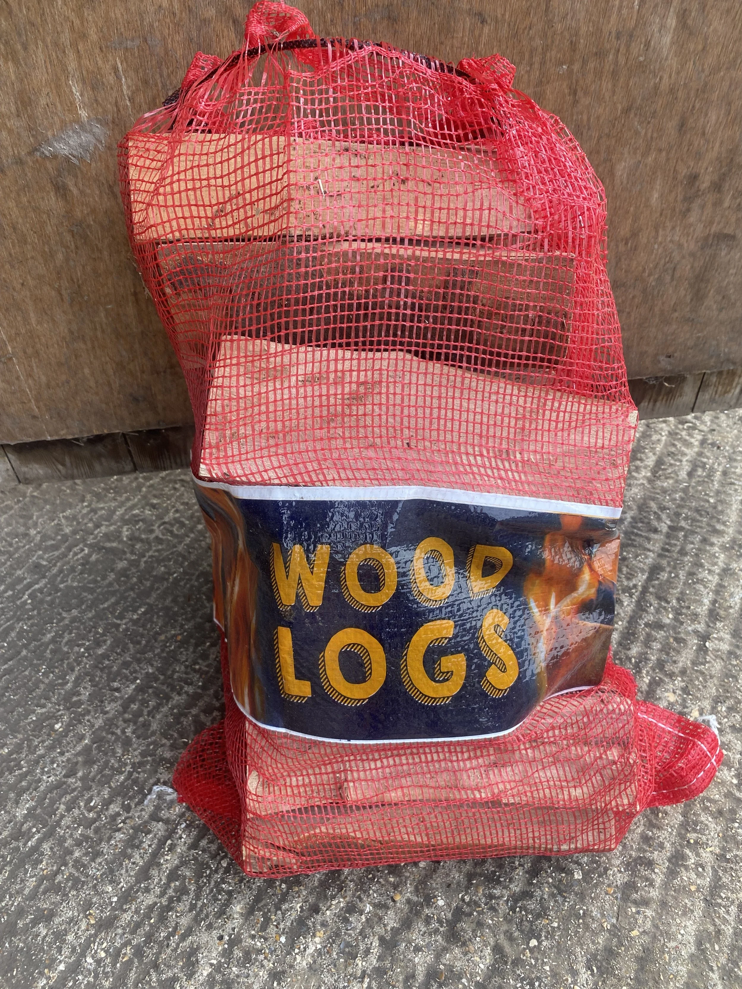 A red mesh outer layer labeled 'Wood Logs' in yellow text, containing chopped wood pieces, placed on a concrete surface against a wooden background.