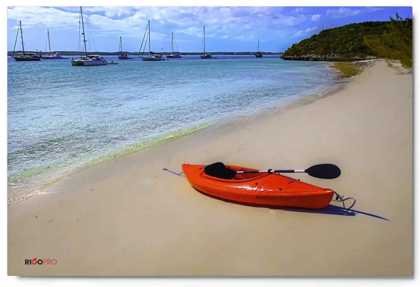 A Caribbean beach scene with a bright red kayak on shore on a smooth sand beach in bright sunlight. The background shows turquoise blue waters and sailboats in the distance, some green-covered rocky shoreline and a blue partly cloudy sky overhead.