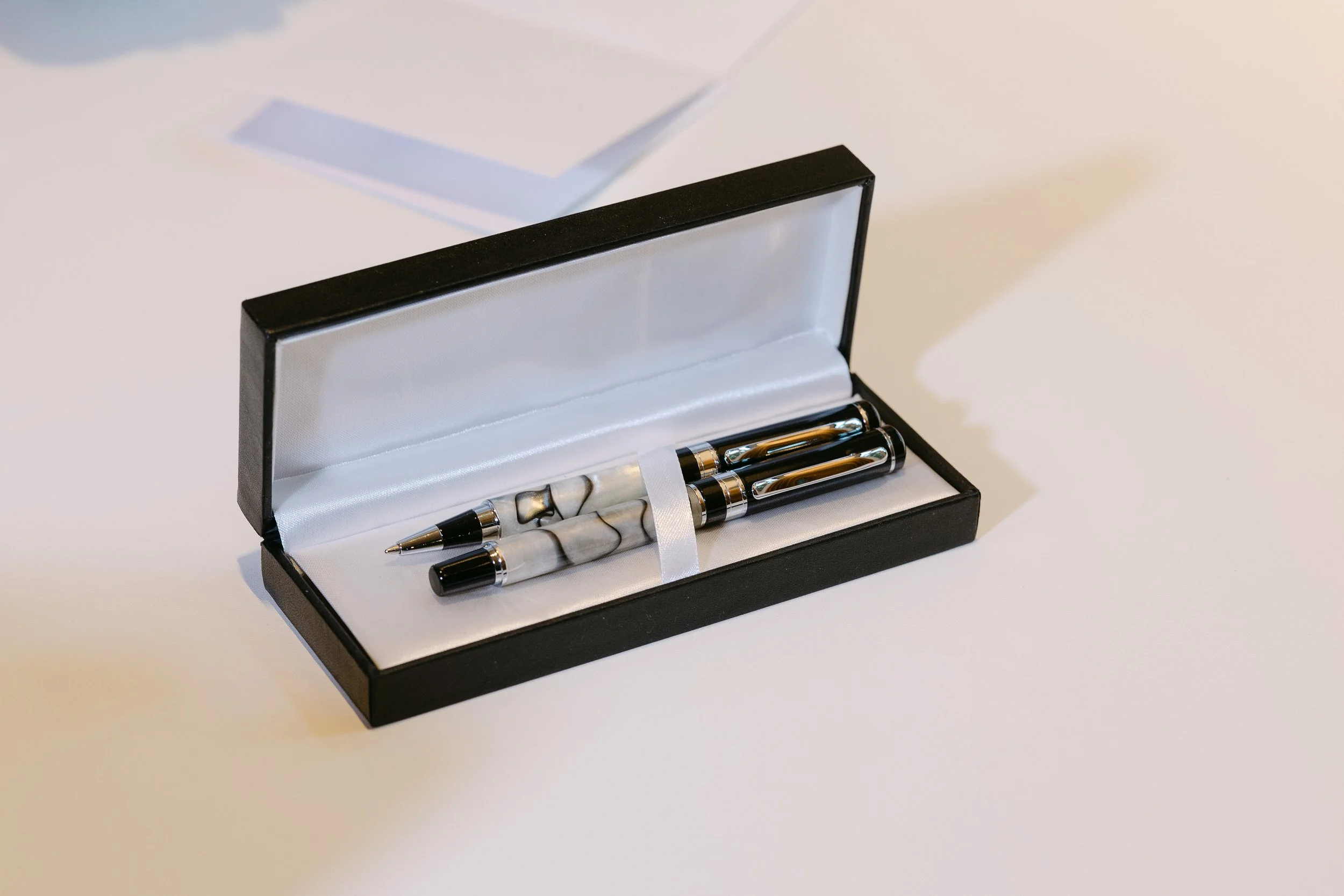A black gift box with a pearl white interior holding a matching black and white marble pen and rollerball pen.