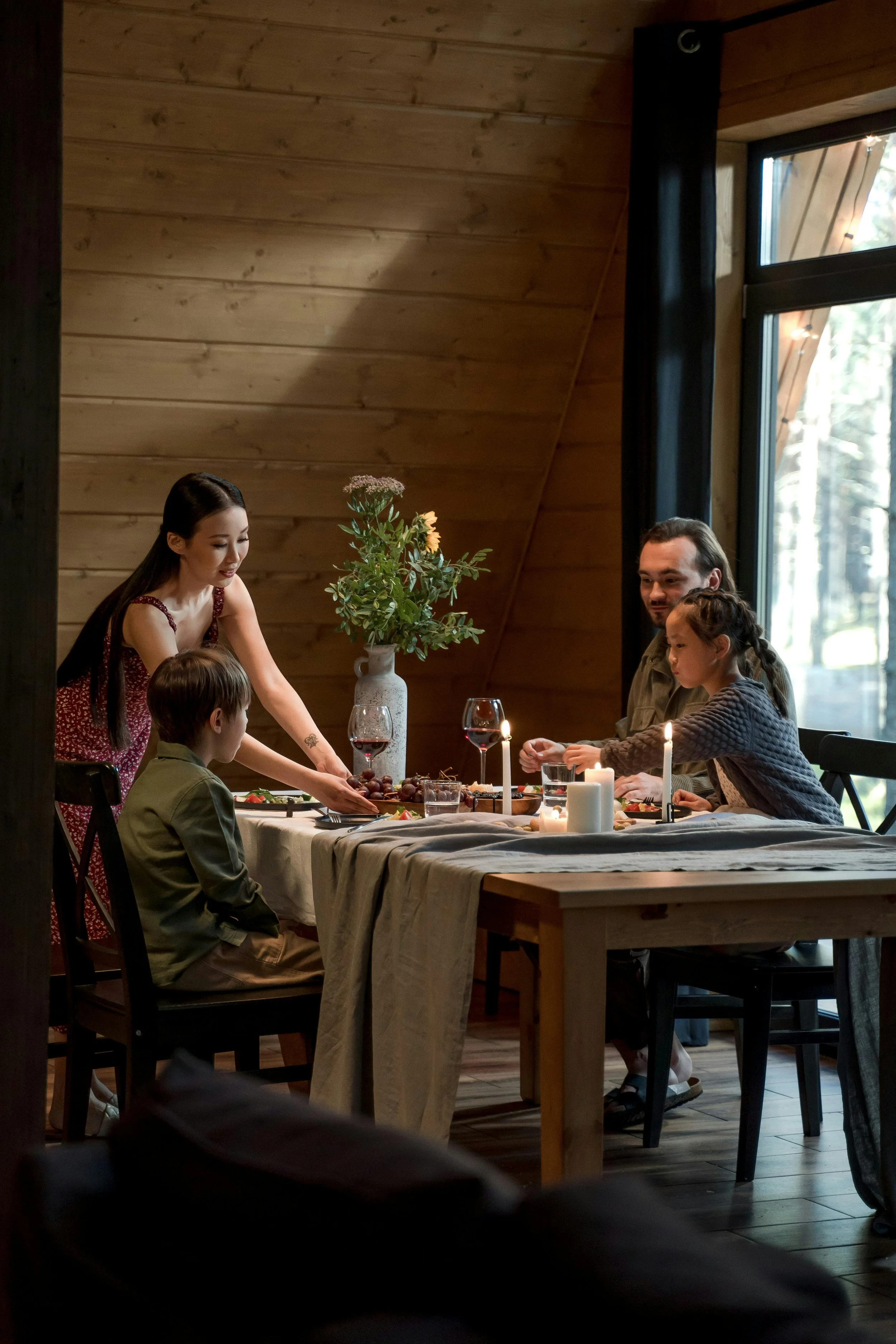 A family enjoying a dinner in a cozy wood-paneled dining room with candles, wine, and a vase of flowers on the table.
