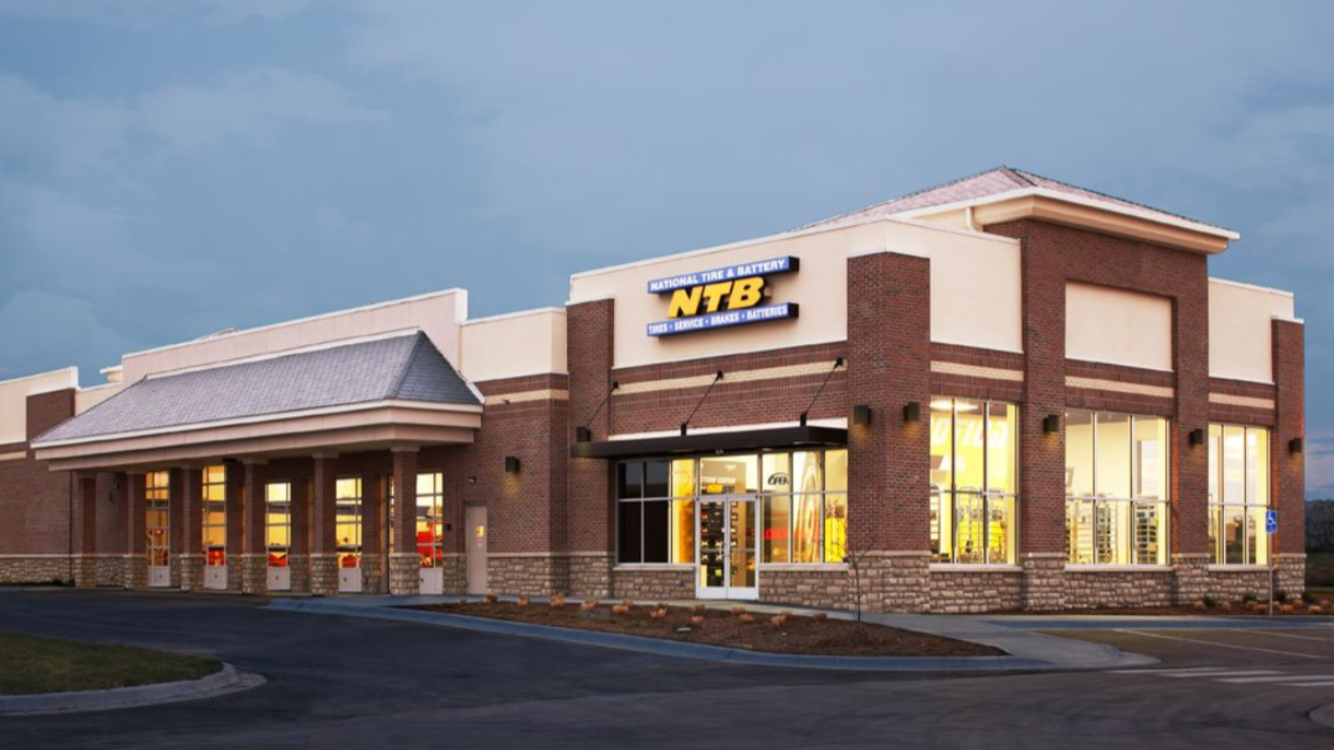 A modern tire and automotive service store with a brick exterior, large glass windows, and a sign that reads 'National Tire & Battery' and 'NTB' outside.