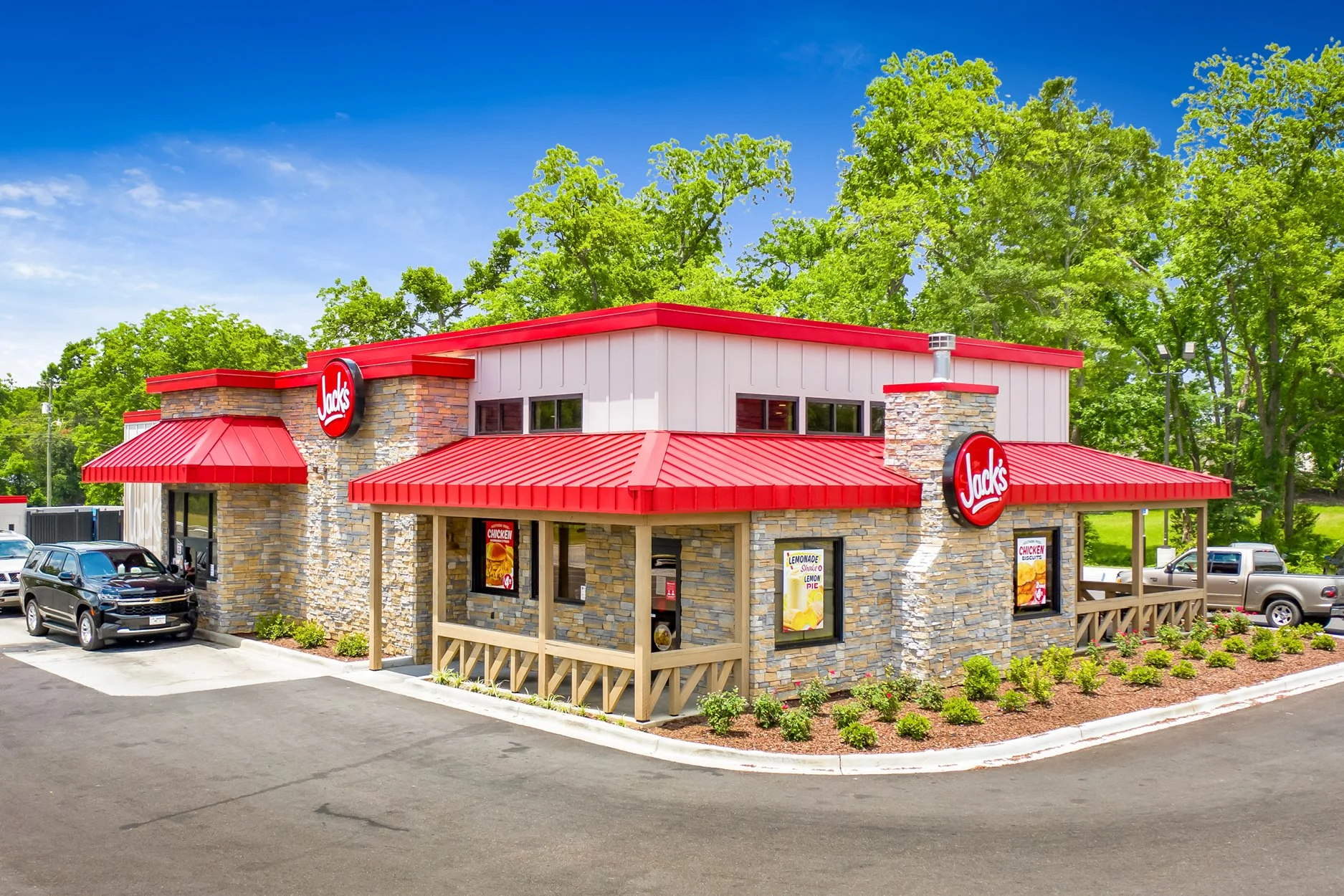 Jack's fast food restaurant with stone exterior, red roof, and signage, surrounded by cars and greenery on a sunny day.