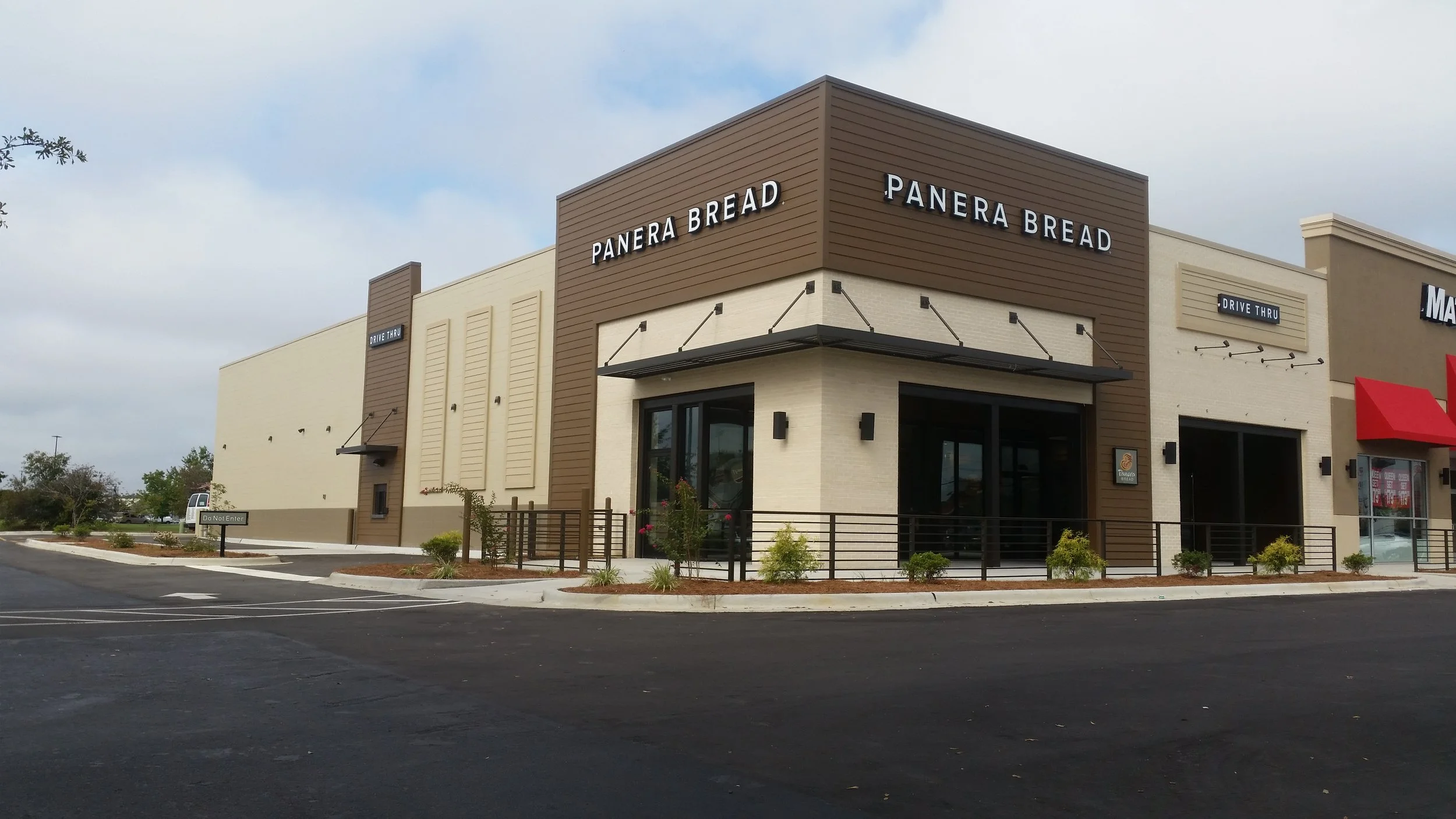 Panera Bread restaurant with a modern design, beige and brown exterior, drive-thru, and parking lot in the foreground.