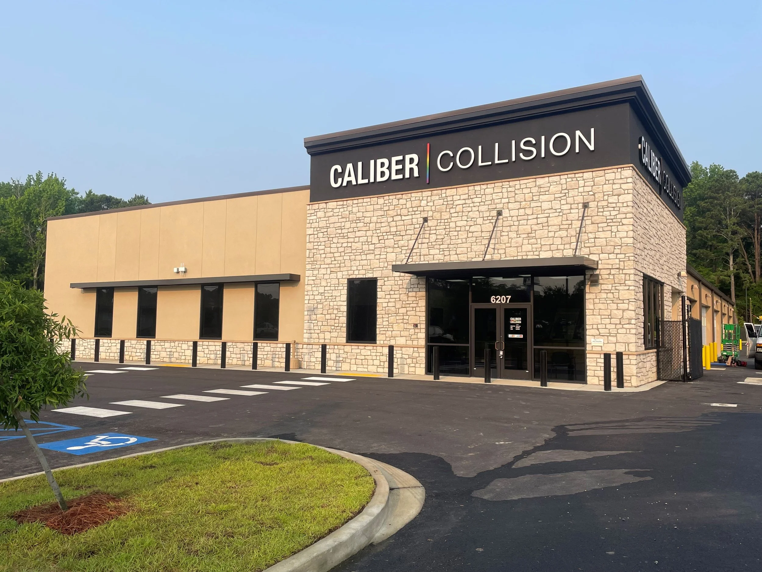 Exterior view of Caliber Collision auto body repair shop with parking lot, handicap parking space, and trees in the background.
