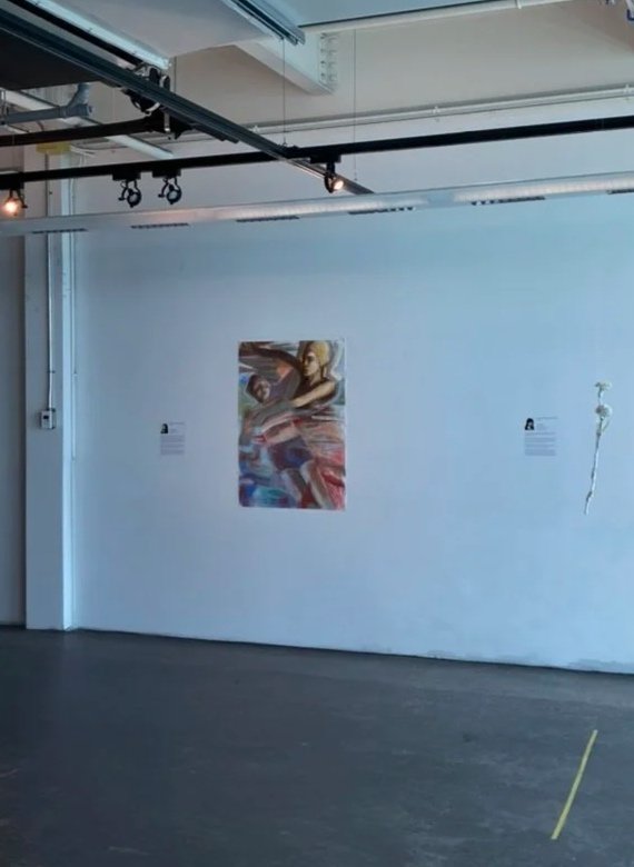Gallery wall with a colorful abstract painting of a woman, a white flower on the right, and two informational plaques on either side of the painting in an art gallery.