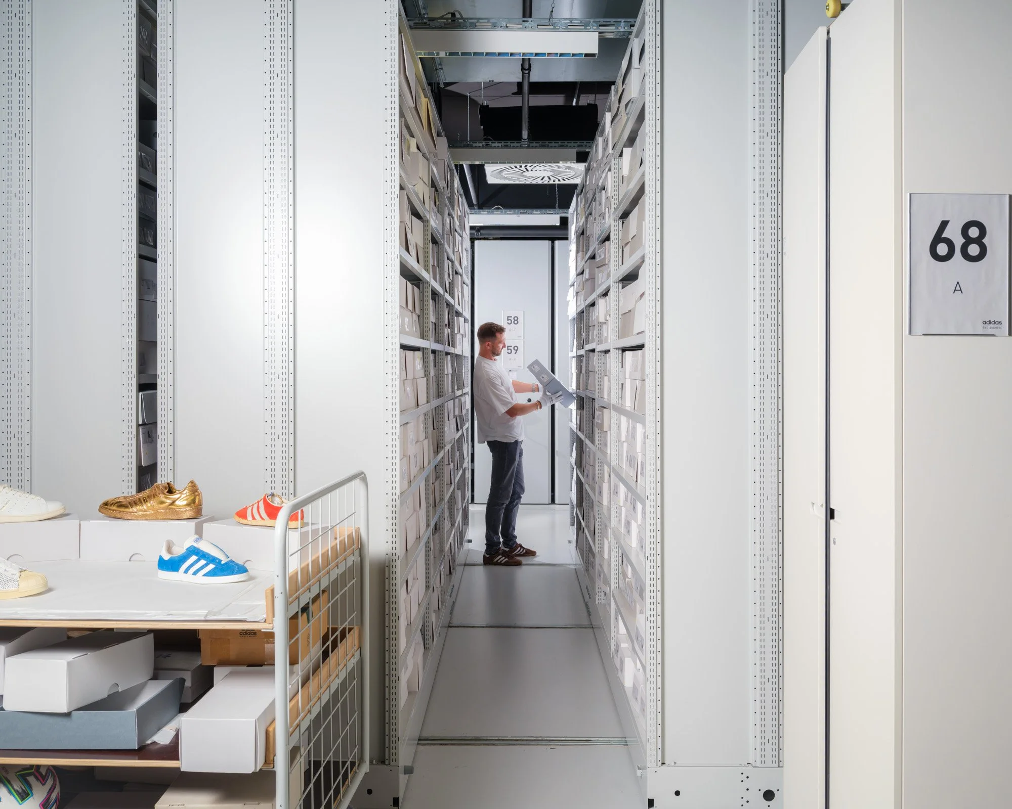 A person standing in an aisle filled with white storage boxes, looking at a clipboard in a storage or warehouse facility.