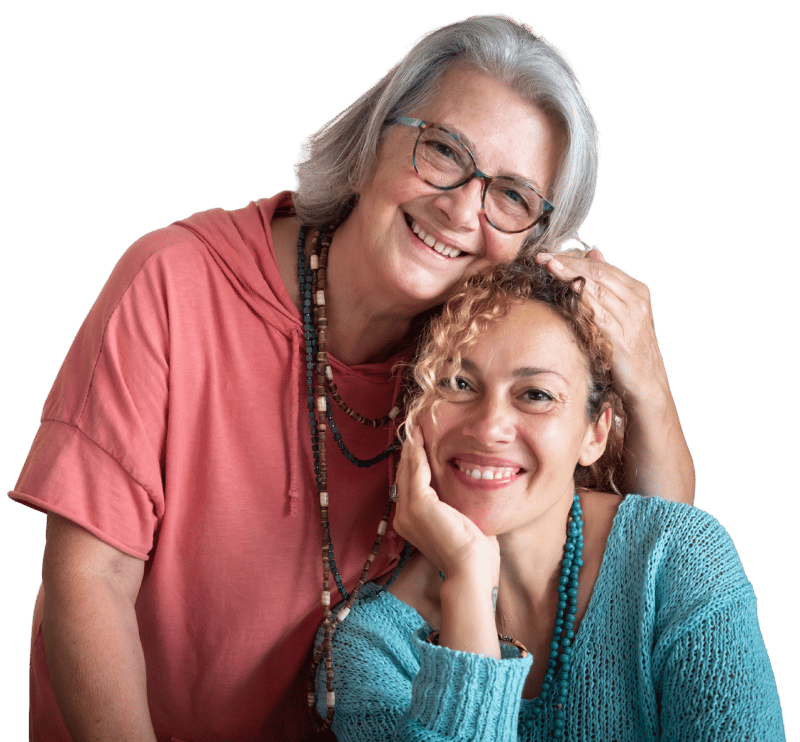 Twee vrouwen glimlachen en poseren samen, waarbij de oudere vrouw troostend haar hand op het hoofd van de jongere vrouw legt.