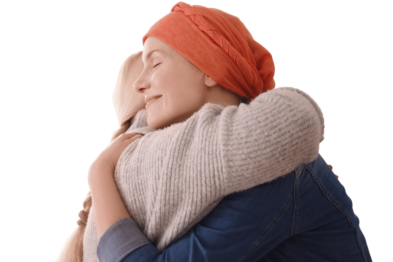 Een vrouw met kanker die troost krijgt van een andere vrouw. De vrouw met kanker draagt een oranje hoofddoek en een beige trui.