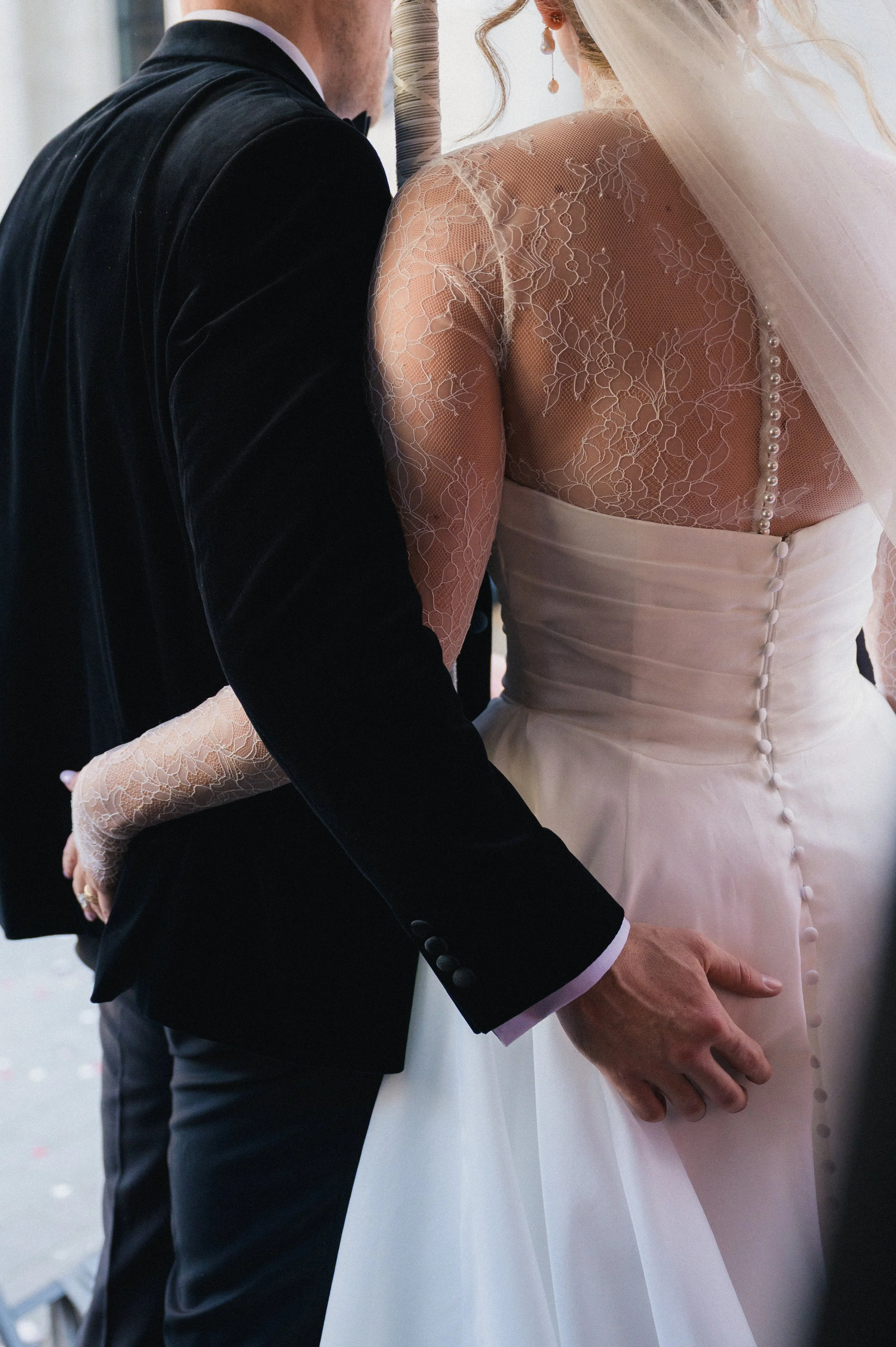 Close-up of a bride and groom holding hands during after wedding ceremony, focusing on their hands and the details of their wedding attire.