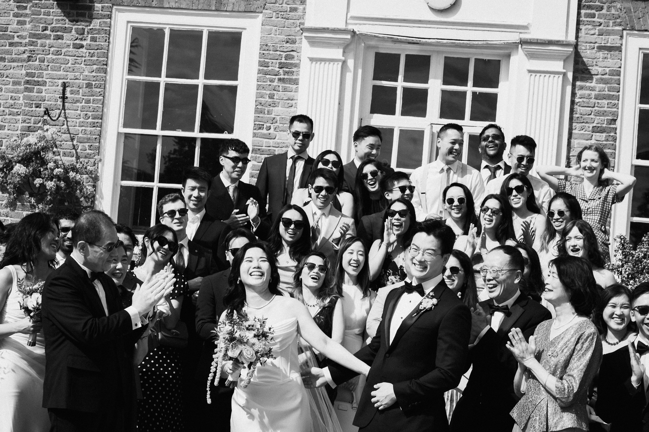 A group of people at a wedding, including the bride and groom, smiling and celebrating outside a building.