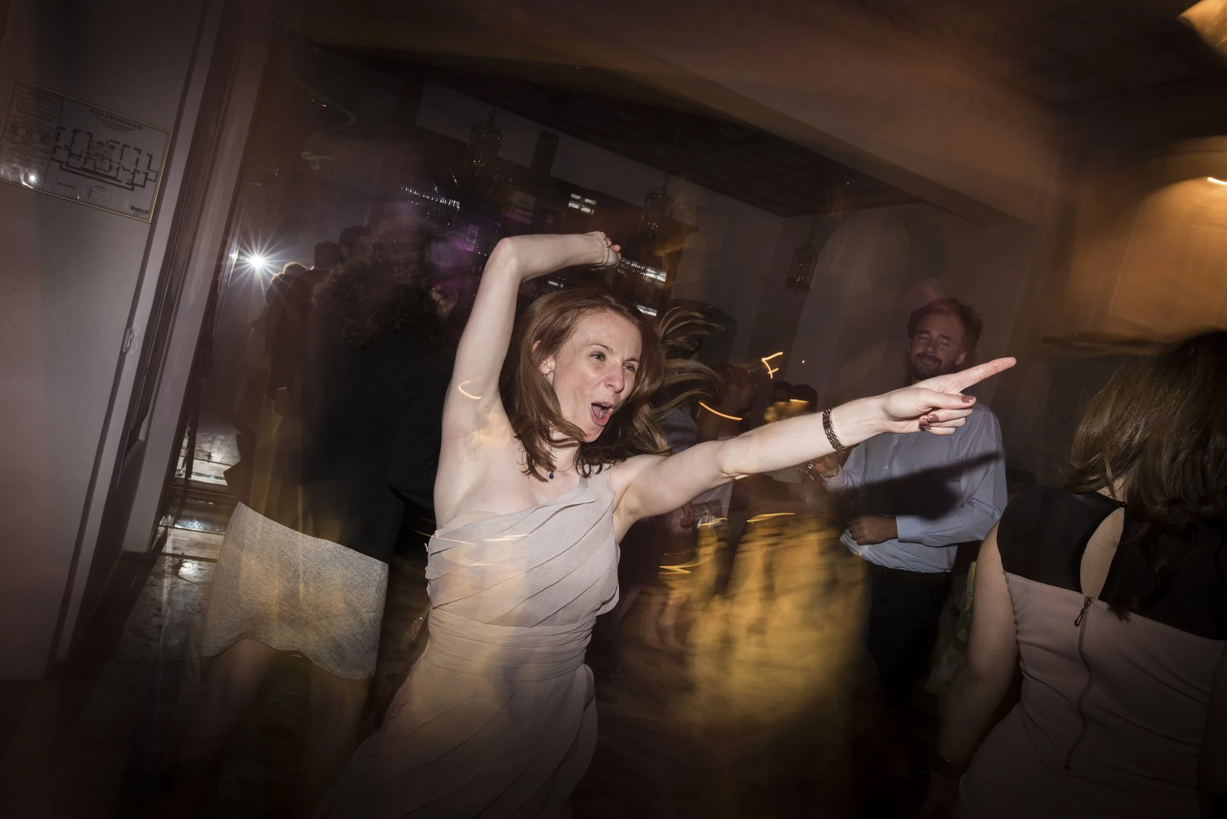 A woman dancing at a party, pointing and making energetic gestures with other guests in the background.