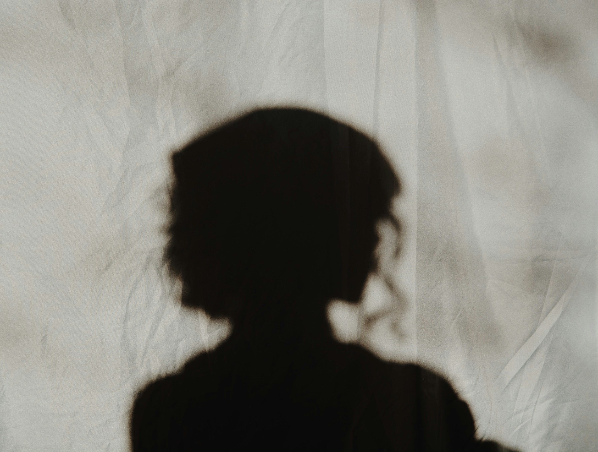 Shadow of a person with curly hair cast onto a crumpled white or light-colored paper background.