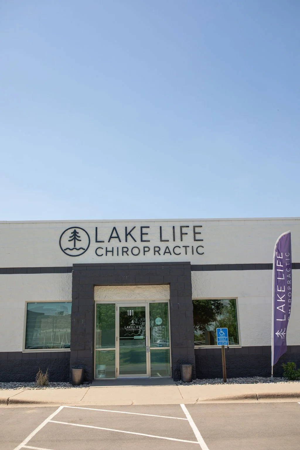 Front view of Lake Life Chiropractic building with an entrance door, a purple flag, and a handicap parking sign