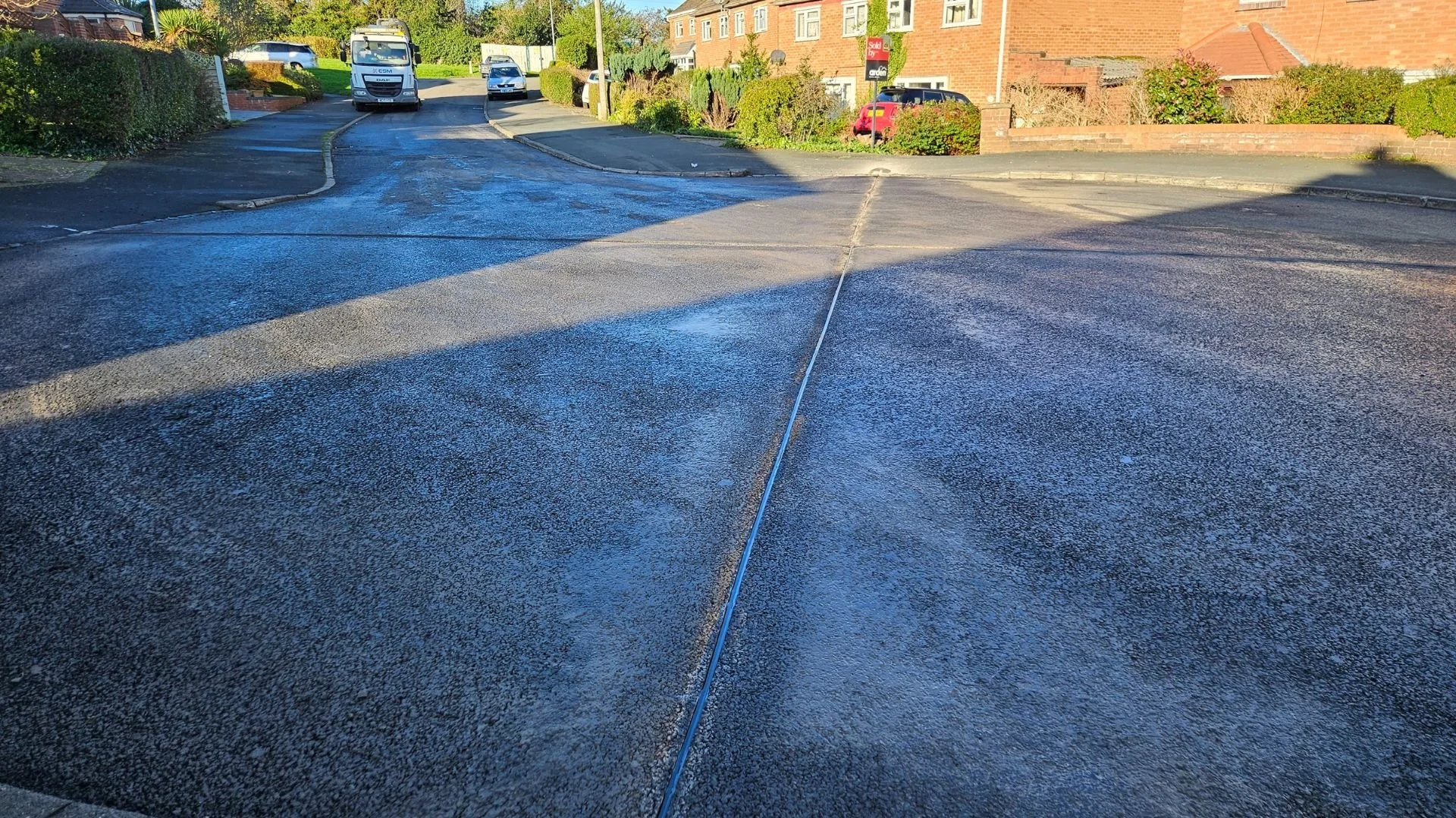 View of a residential street intersection with a road with newly completed sealant