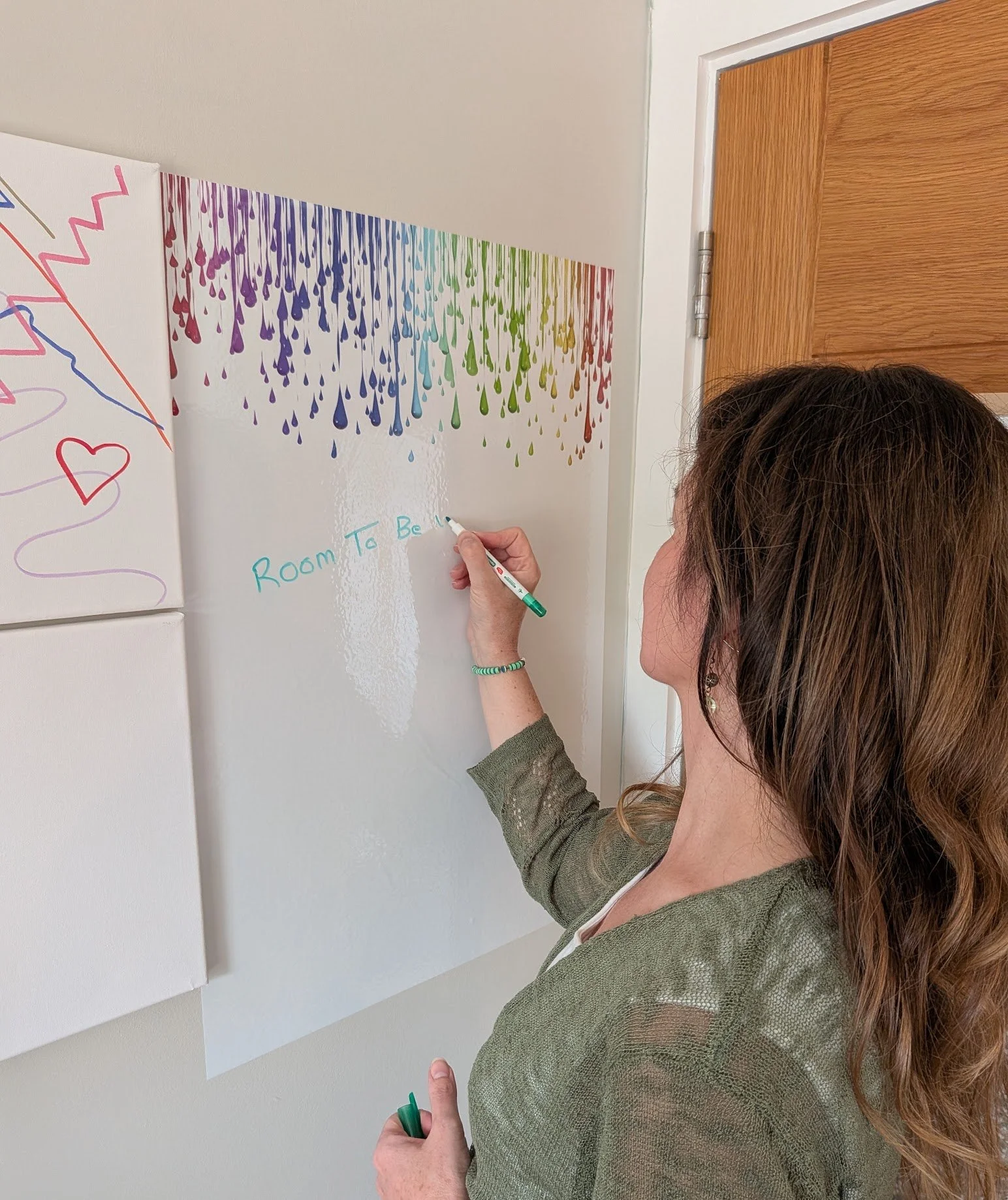 Therapist writing on a rainbow coloured whiteboard inside her therapy room in Mawdesley, Lancashire