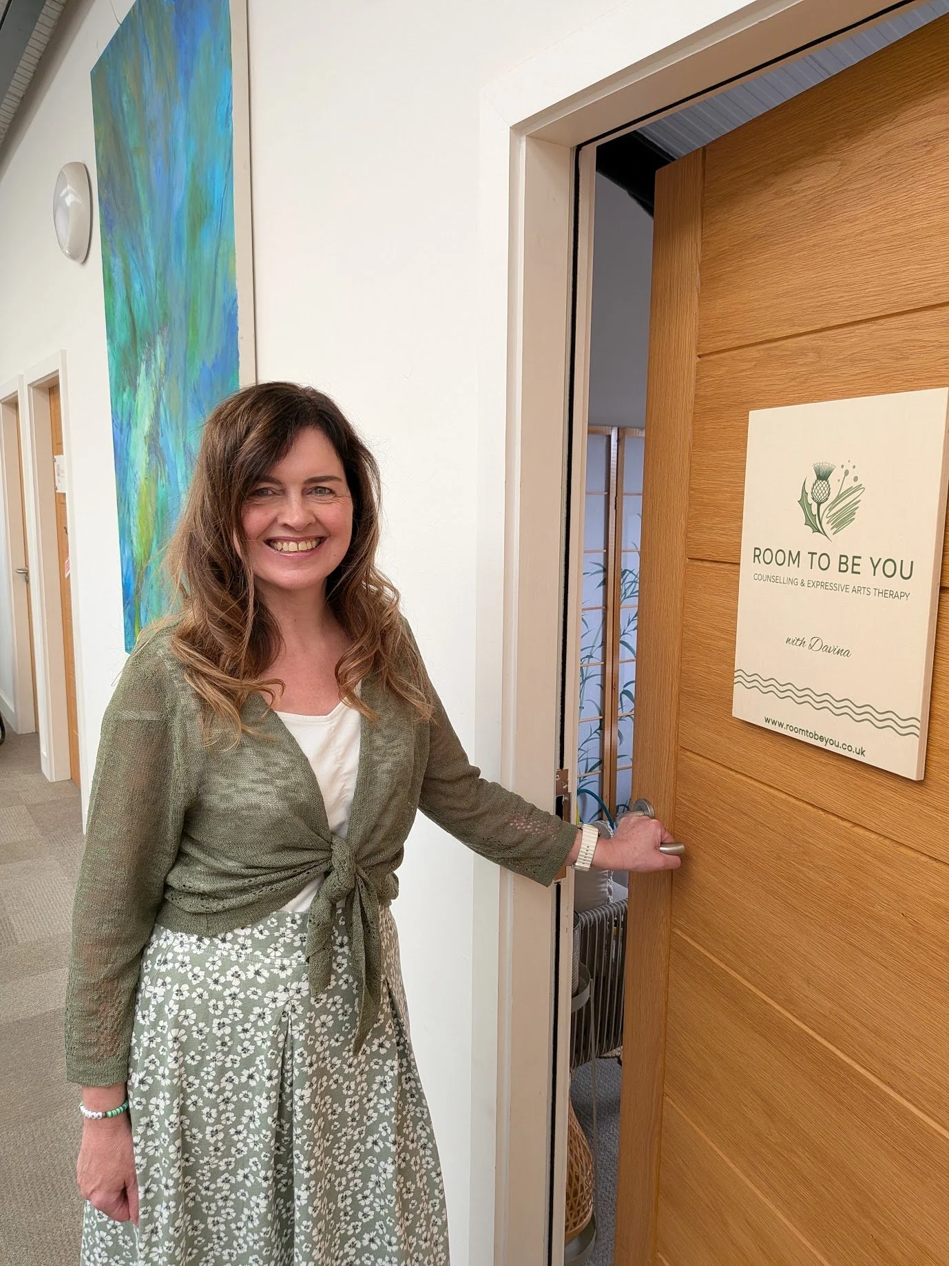 Therapist Davina Hanlon outside her therapy room with a sign saying 'Room to Be You' for counselling and expressive arts therapy. 