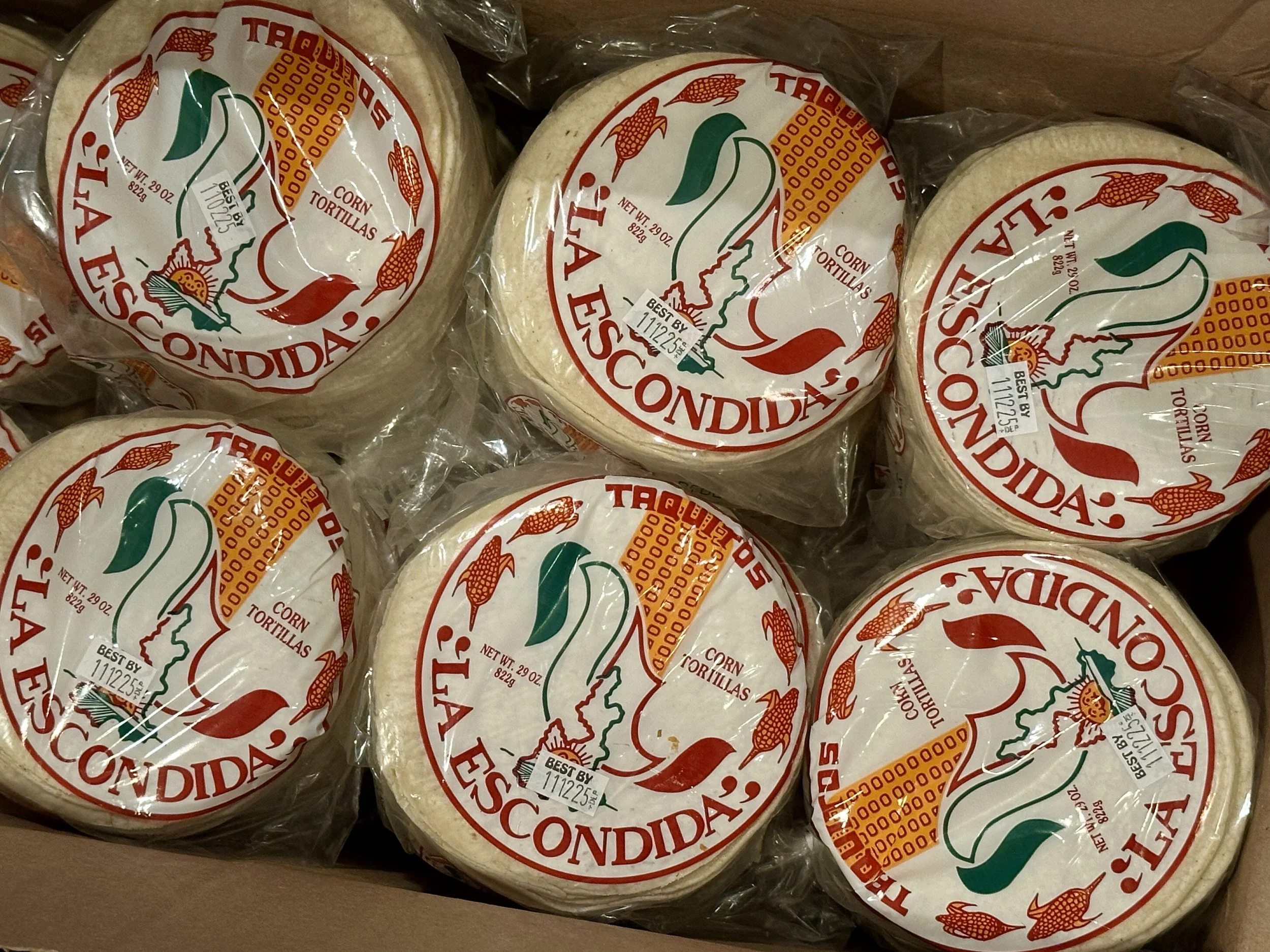 Six packages of La Escondida corn tortillas in plastic wrapping inside a cardboard box.