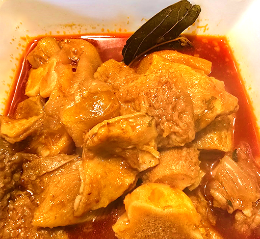 A dish of chicken cooked in a tomato-based sauce with onion pieces and a bay leaf garnished with a whole bay leaf.