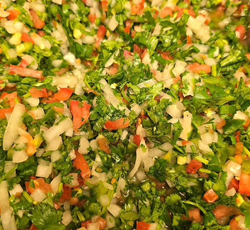 Close-up of chopped mixed vegetables, including green leafy herbs, red and yellow diced peppers, and chopped onion.