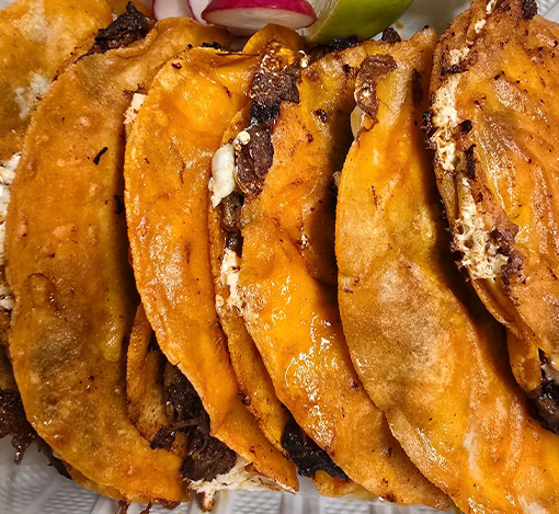 Close-up of crispy fried tacos filled with meat and cheese.