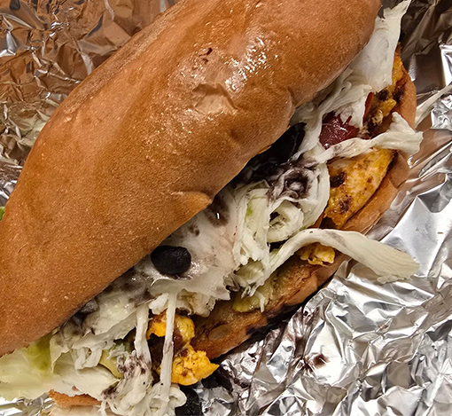 Sub sandwich with lettuce, black beans, scrambled eggs, and sauce in a toasted bun, wrapped in foil.