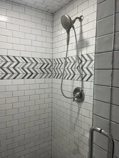 Modern matte-black shower fixtures and handheld sprayer on white subway tile with chevron band – Harrisville, UT remodel by VCON Remodeling & Restoration