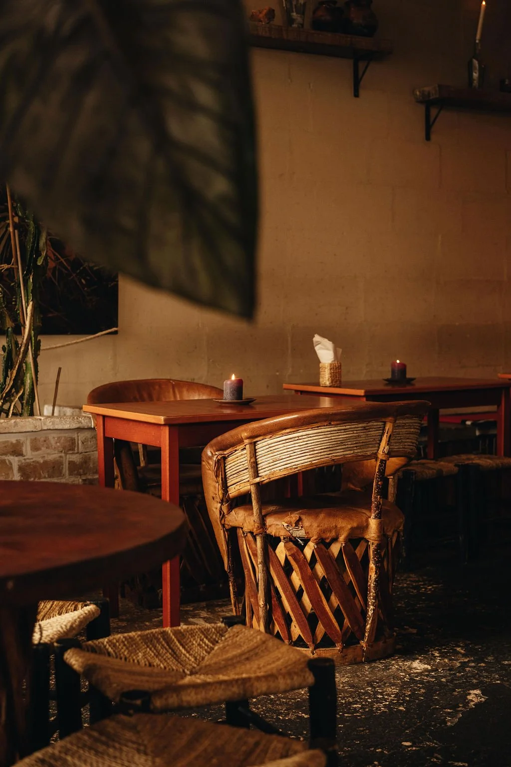 Cozy restaurant interior with wooden tables, wicker chairs, lit candles, tissue box, and warm ambient lighting.