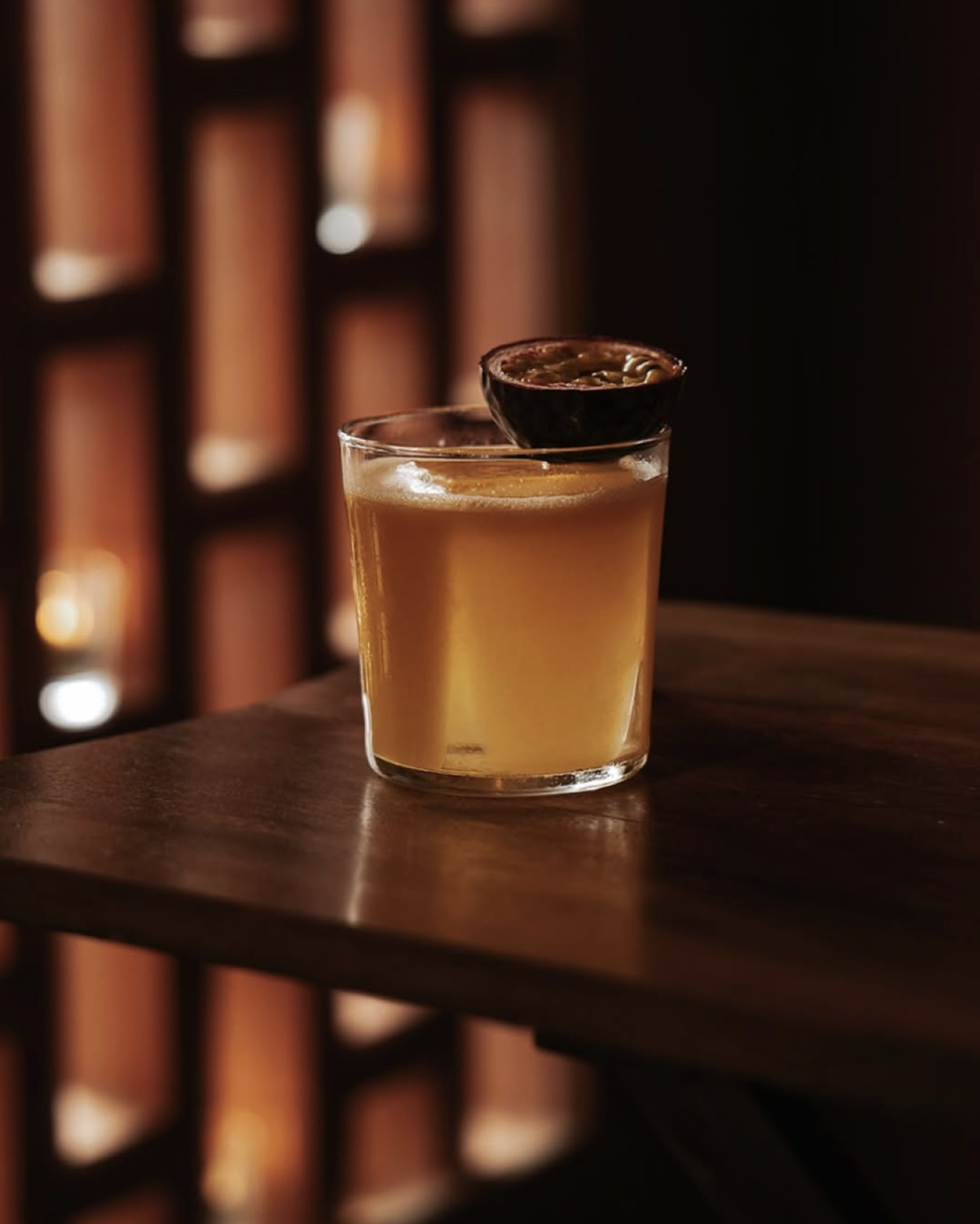 A glass of whiskey with a small bowl of snack on top, placed on a wooden table in a dimly lit setting.