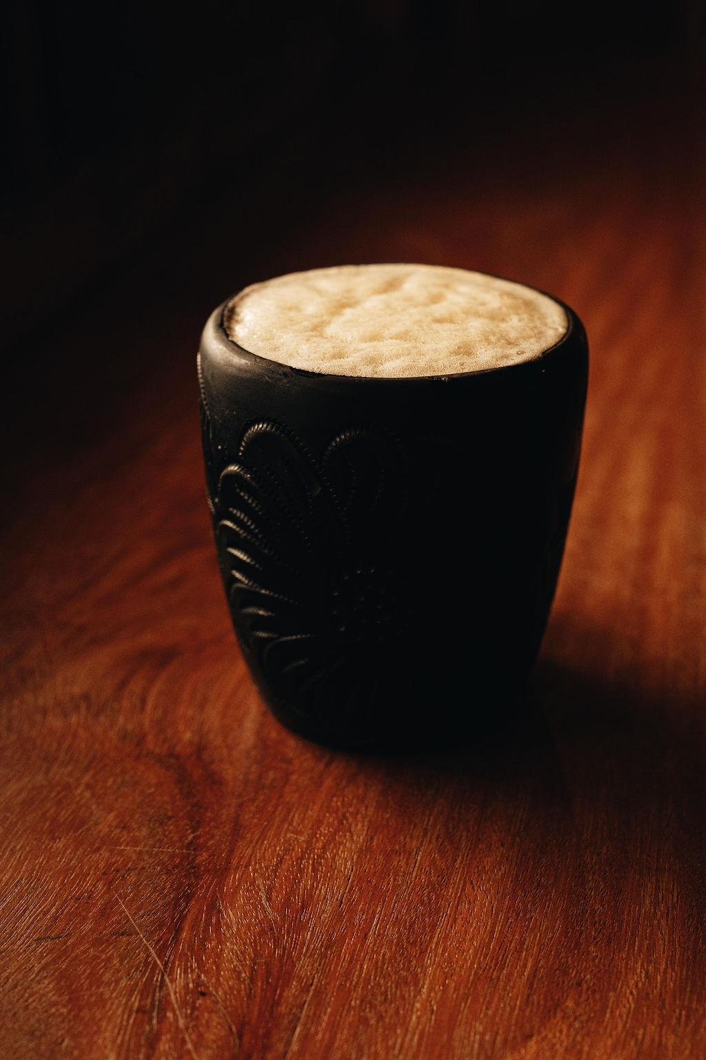 A black cup with decorative designs filled with a frothy beverage, placed on a wooden surface.