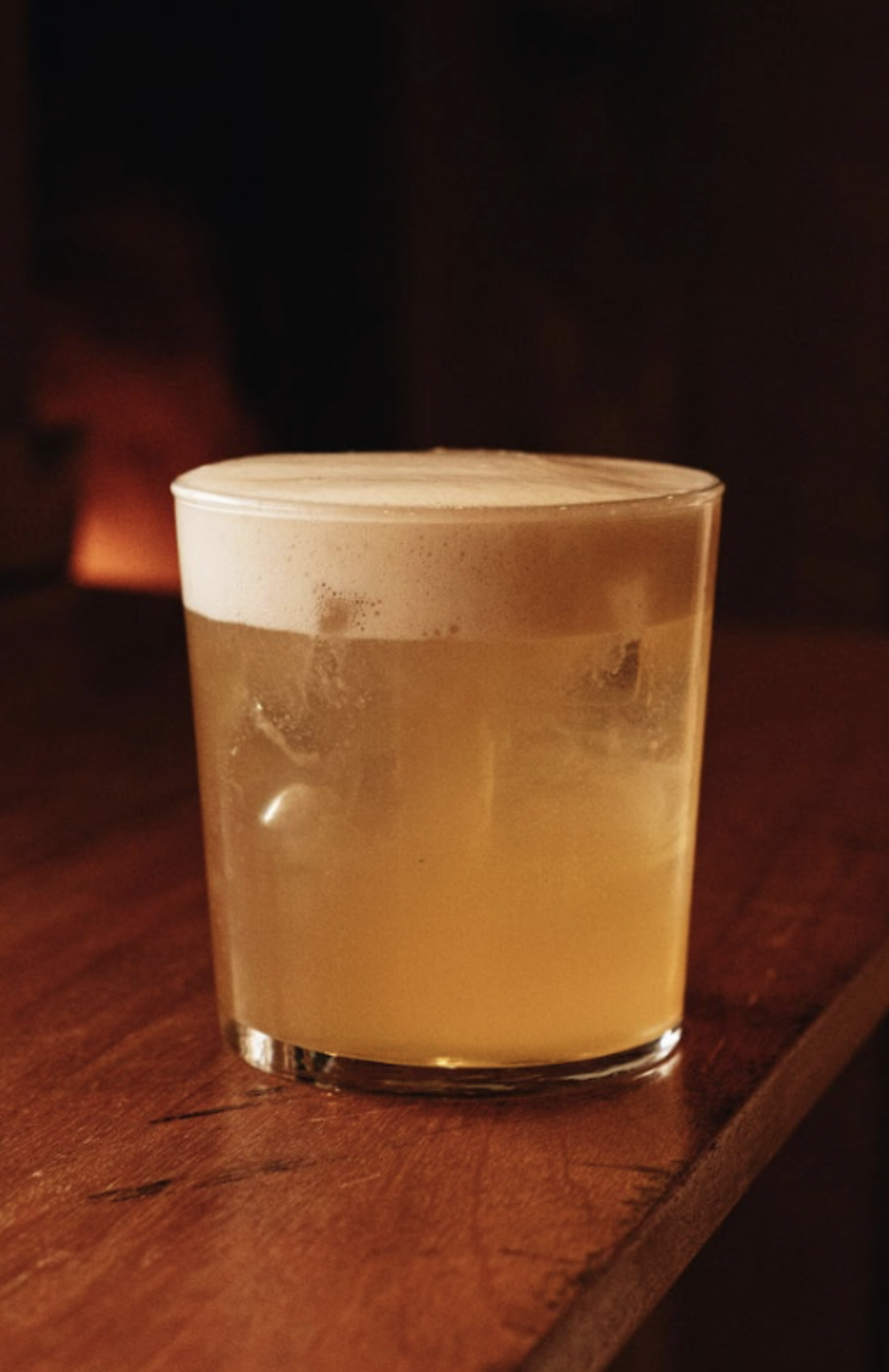 A glass of beer on a wooden table in a dimly lit setting.