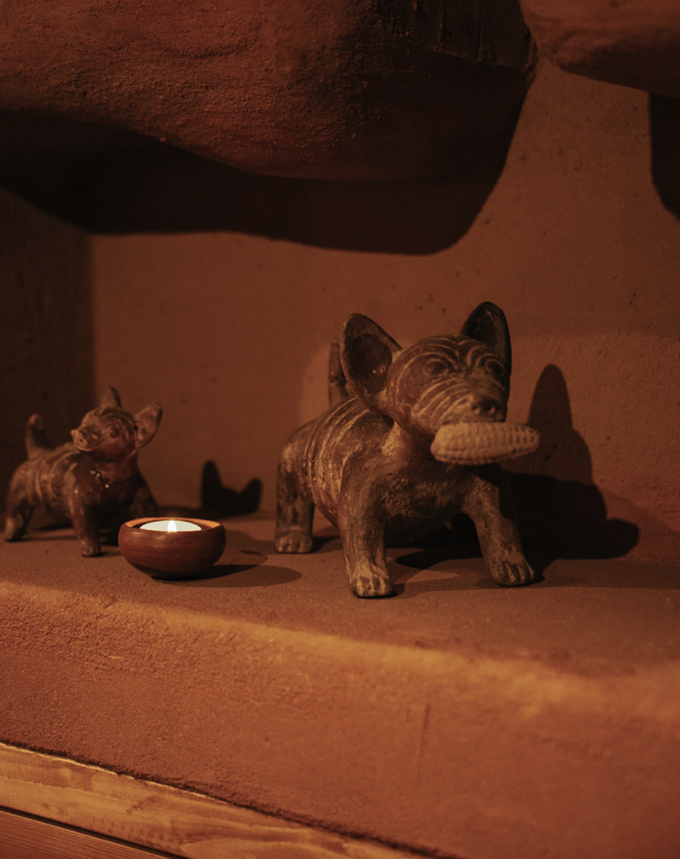 Interior scene with African-style animal figurines, including an elephant and a dog, lit by a candle on a warm-toned surface.