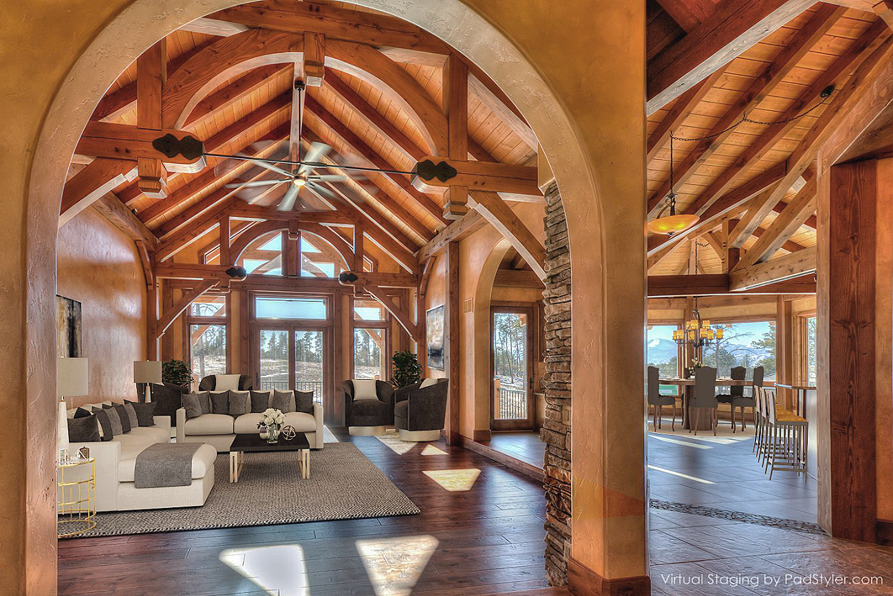Living room with high wooden vaulted ceiling, large windows, white sectional sofa, armchairs, coffee table, and dining area visible in the background.