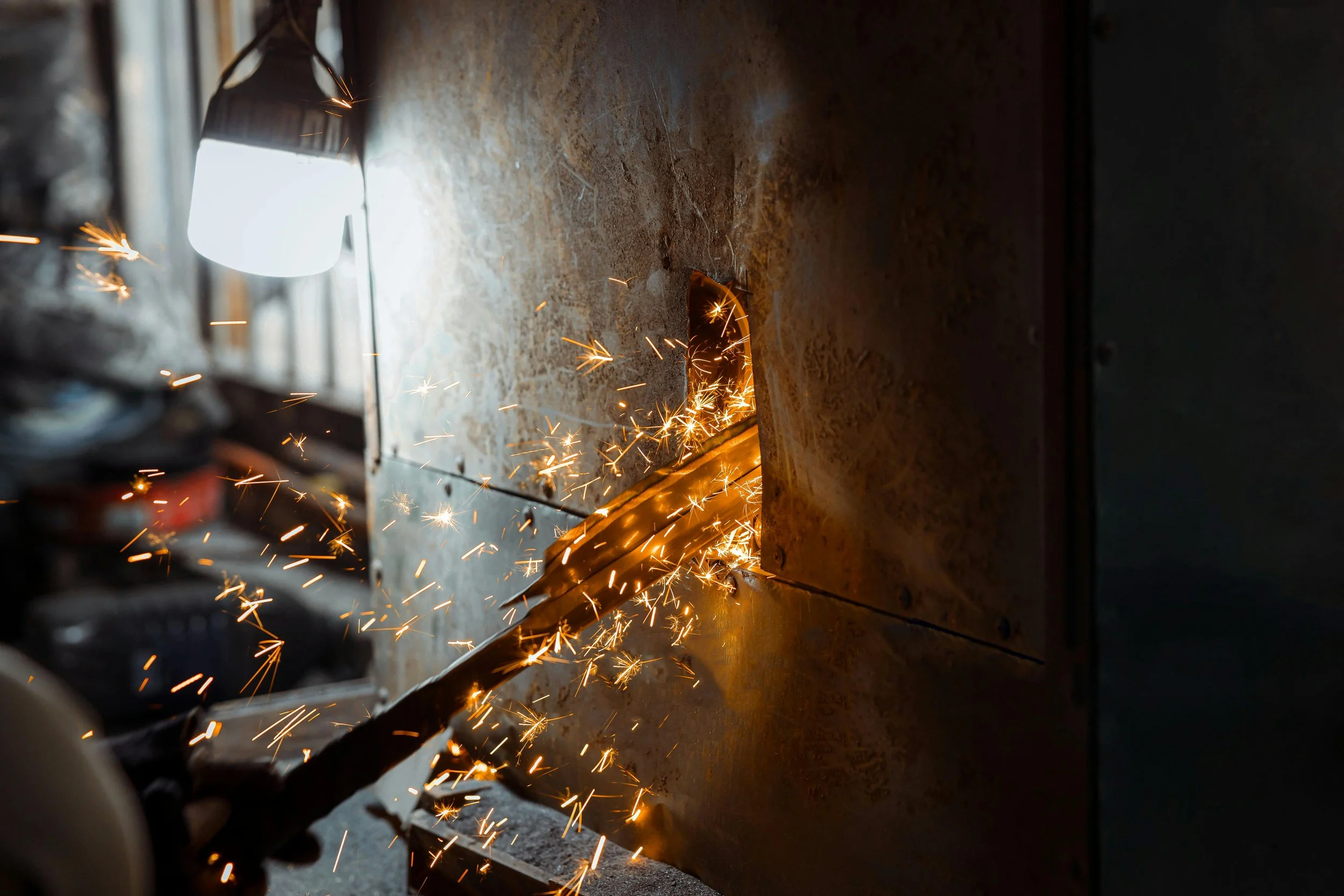 Schweißen eines Metallstücks mit Funkenflug in einer Werkstatt.