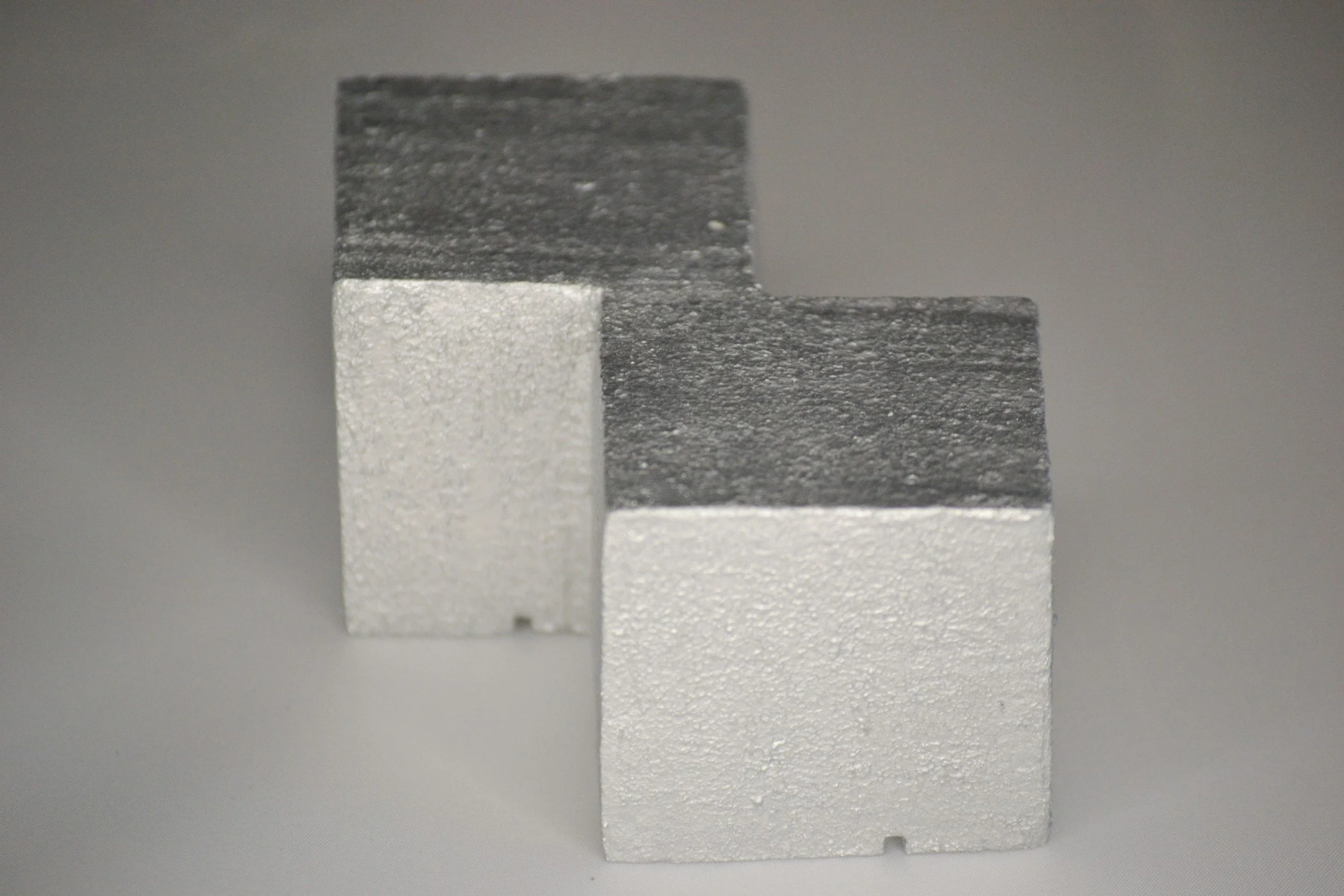 Zwei Metallstücke, eines silberfarben und eines dunkler, übereinandergelegt, auf einer grauen Oberfläche.